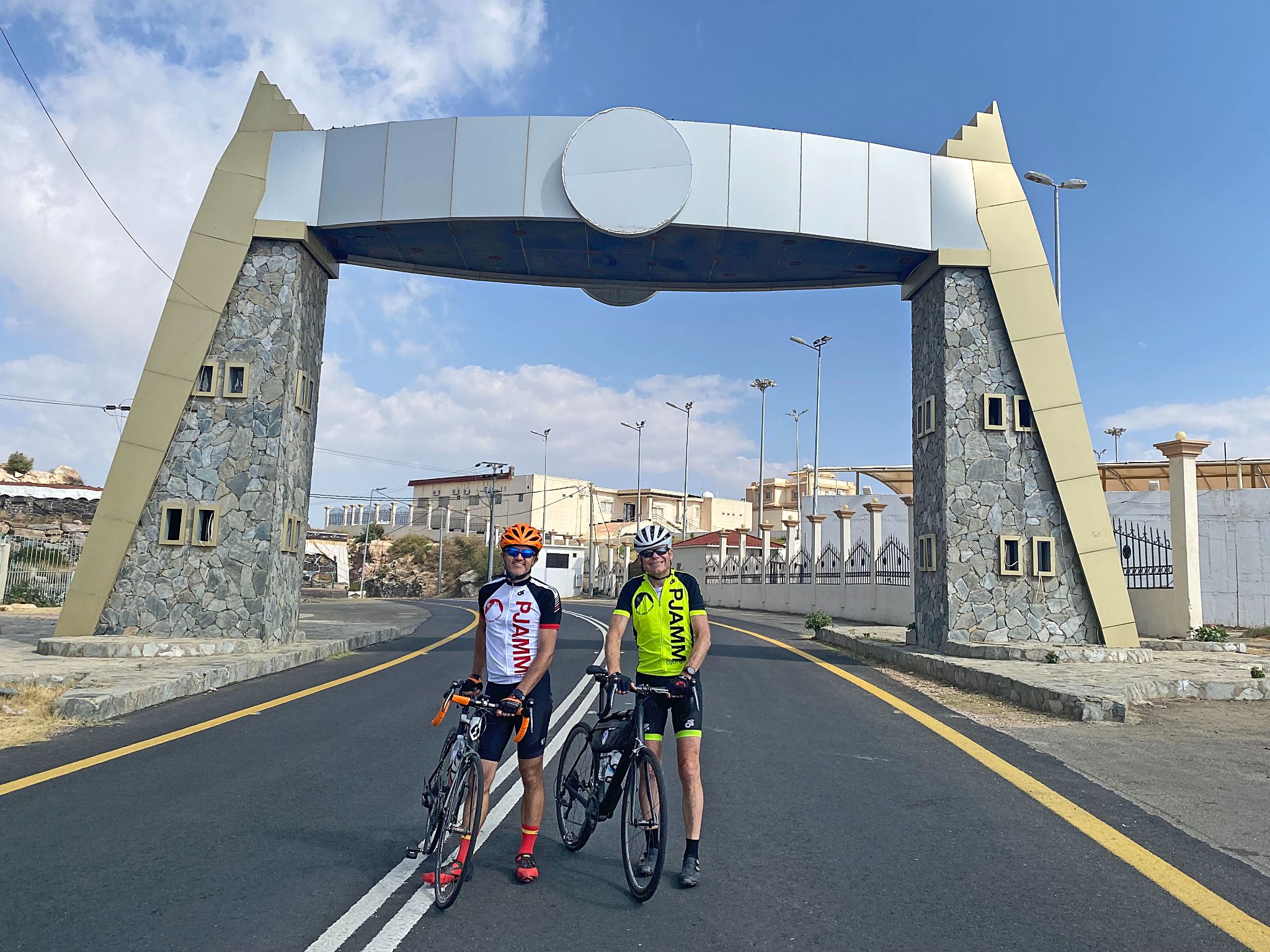Cycling Parmah Pass, Saudi Arabia  - two PJAMM Cyclists stand with bikes under bridge structure crossing roadway at climb's finish