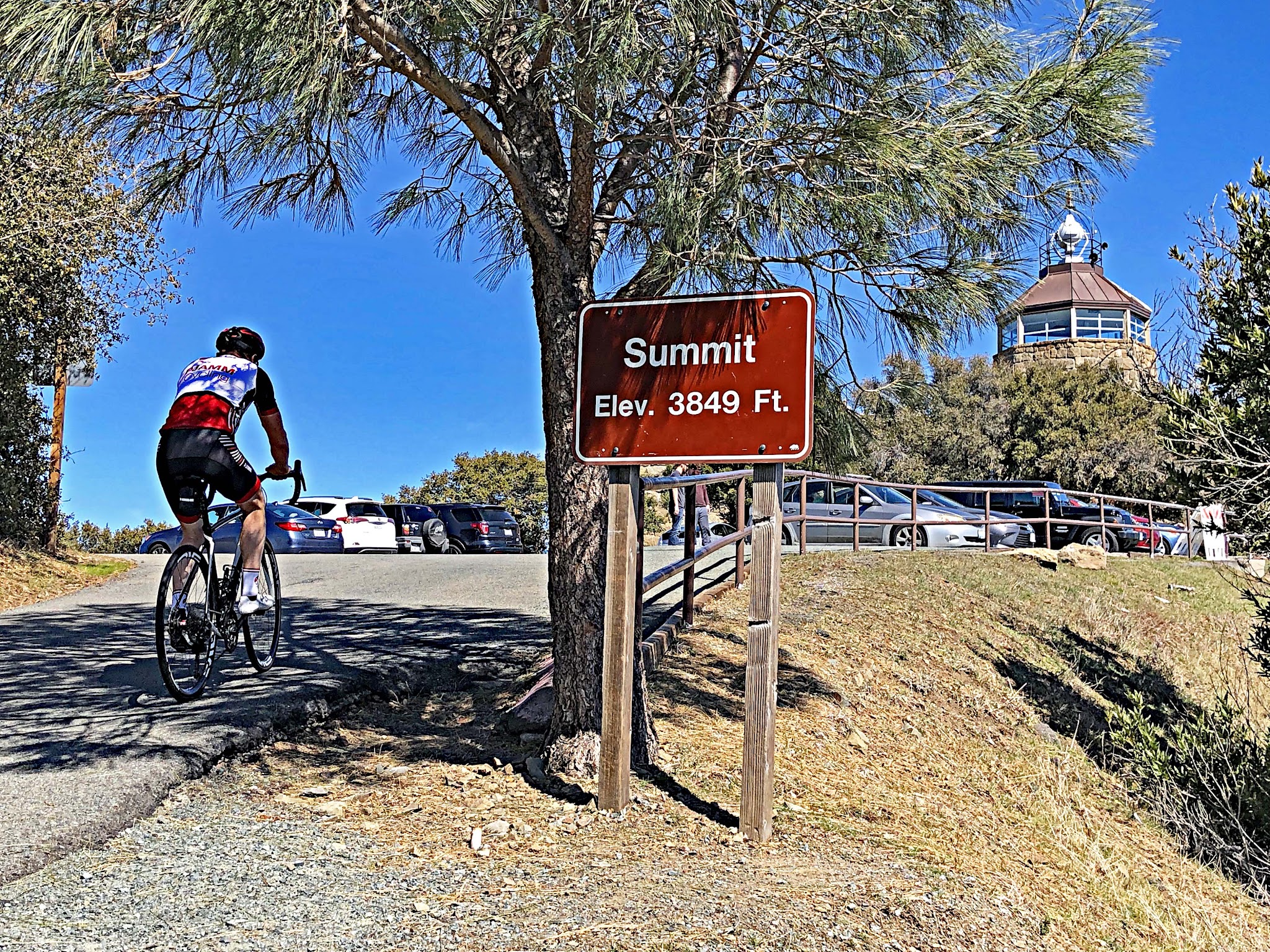 Cycling Mt. Diablo - cyclist on bike riding past summit sign - visitor center and beacon