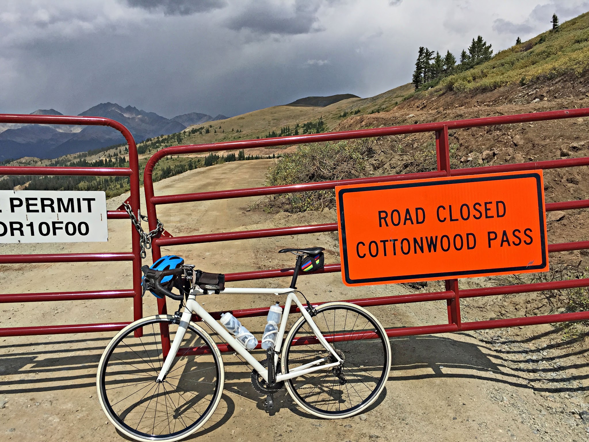 Cycling Cottonwood Pass, Colorado - pre-paving of back side of pass prior to 2019, bike parked against red gate closing off dirt portion of road