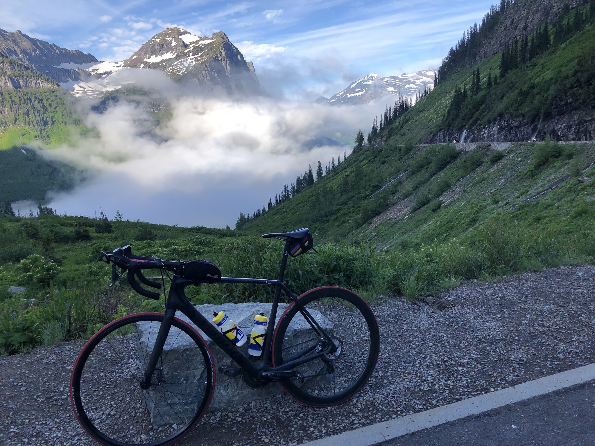 Cycling Going to the Sun Road - Logan Pass - bicycle leaning against guardrail, clouds mountains, forest