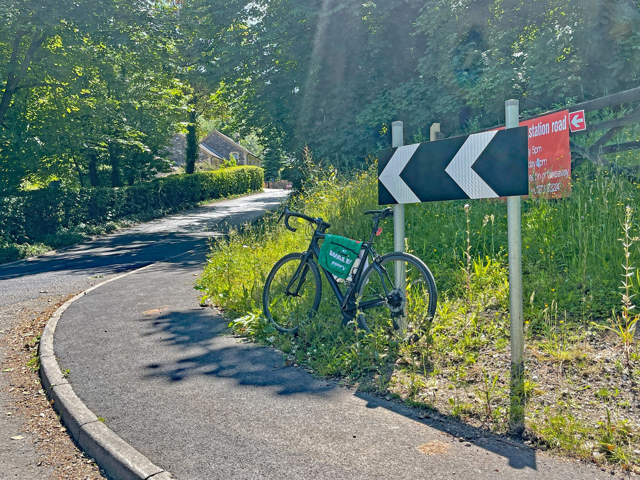 bike parked in grass next to sidewalk, against sign for curve in roadway