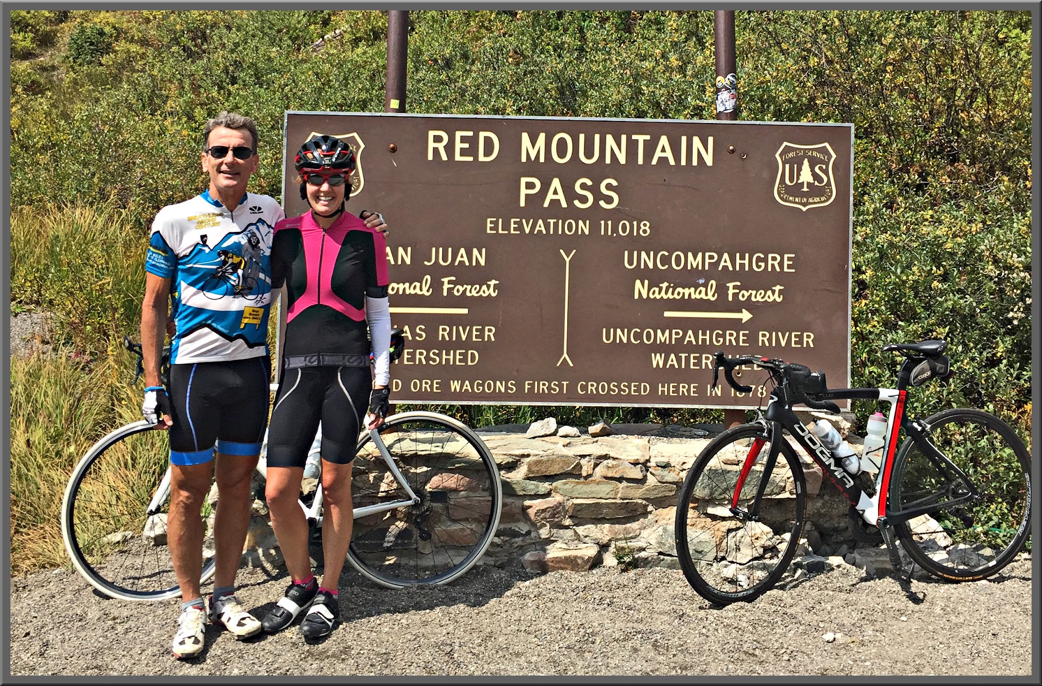 Cycling Red Mountain,  Ouray, Colorado - two cyclists with their bikes standing in front of sign for Red Mountain Pass, Elevation 11,018