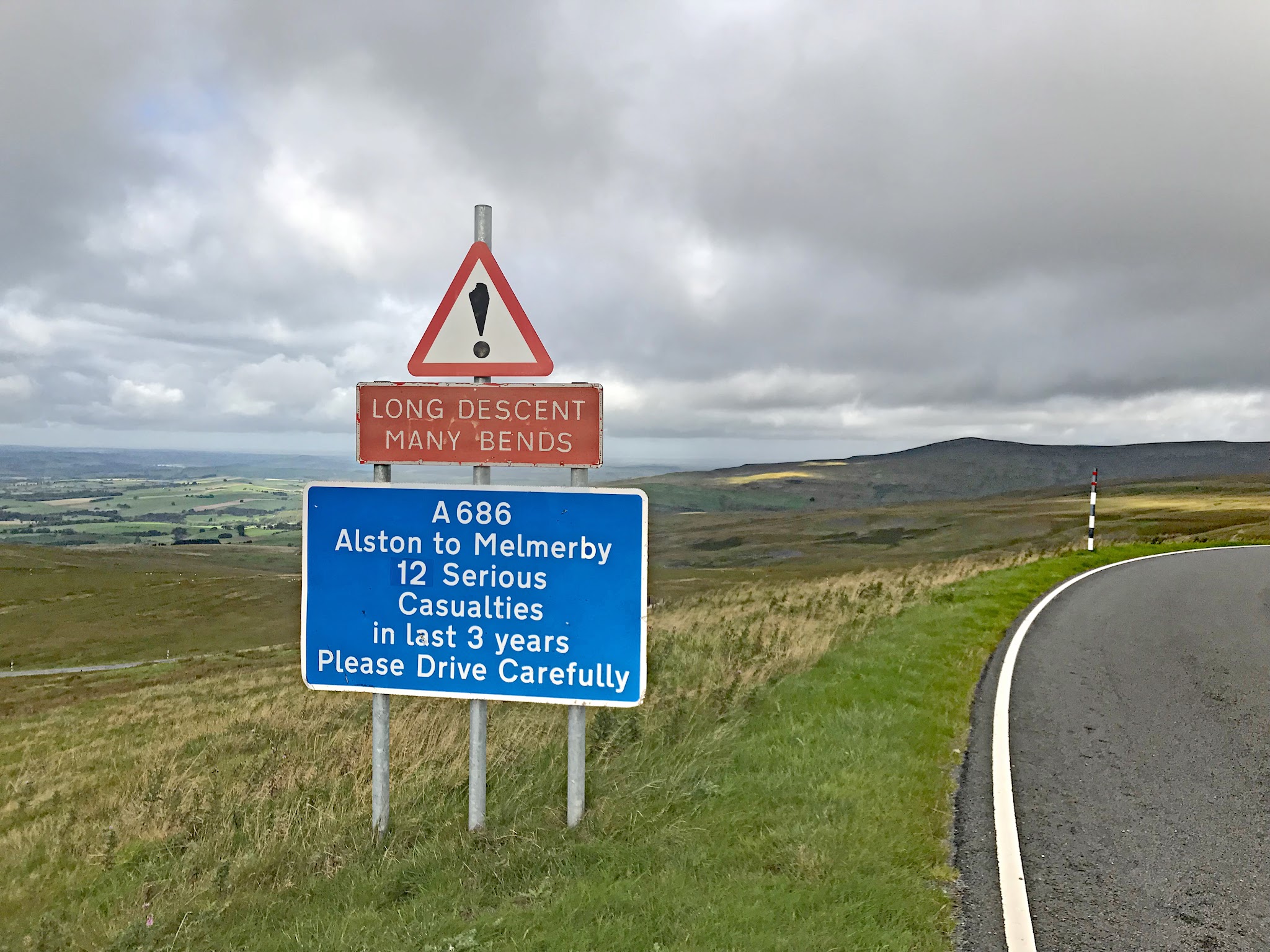 Cycling Hartside, UK - road sign warning of long descent, many bends, curved road with pastureland alongside it