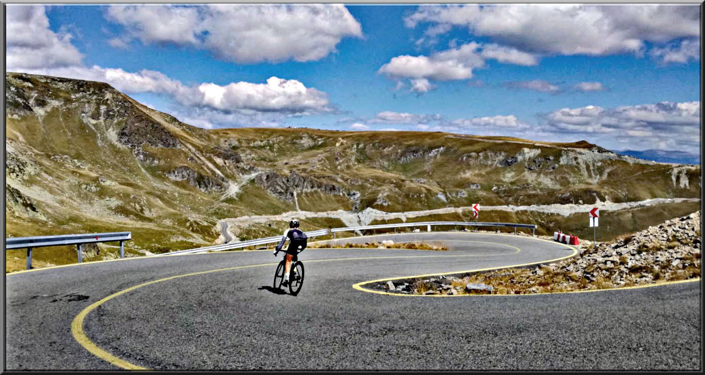 Cycling Transalpina North, Romania - cyclist rides down winding two-lane highway roadway in Romanian alps, blue sky and white clouds