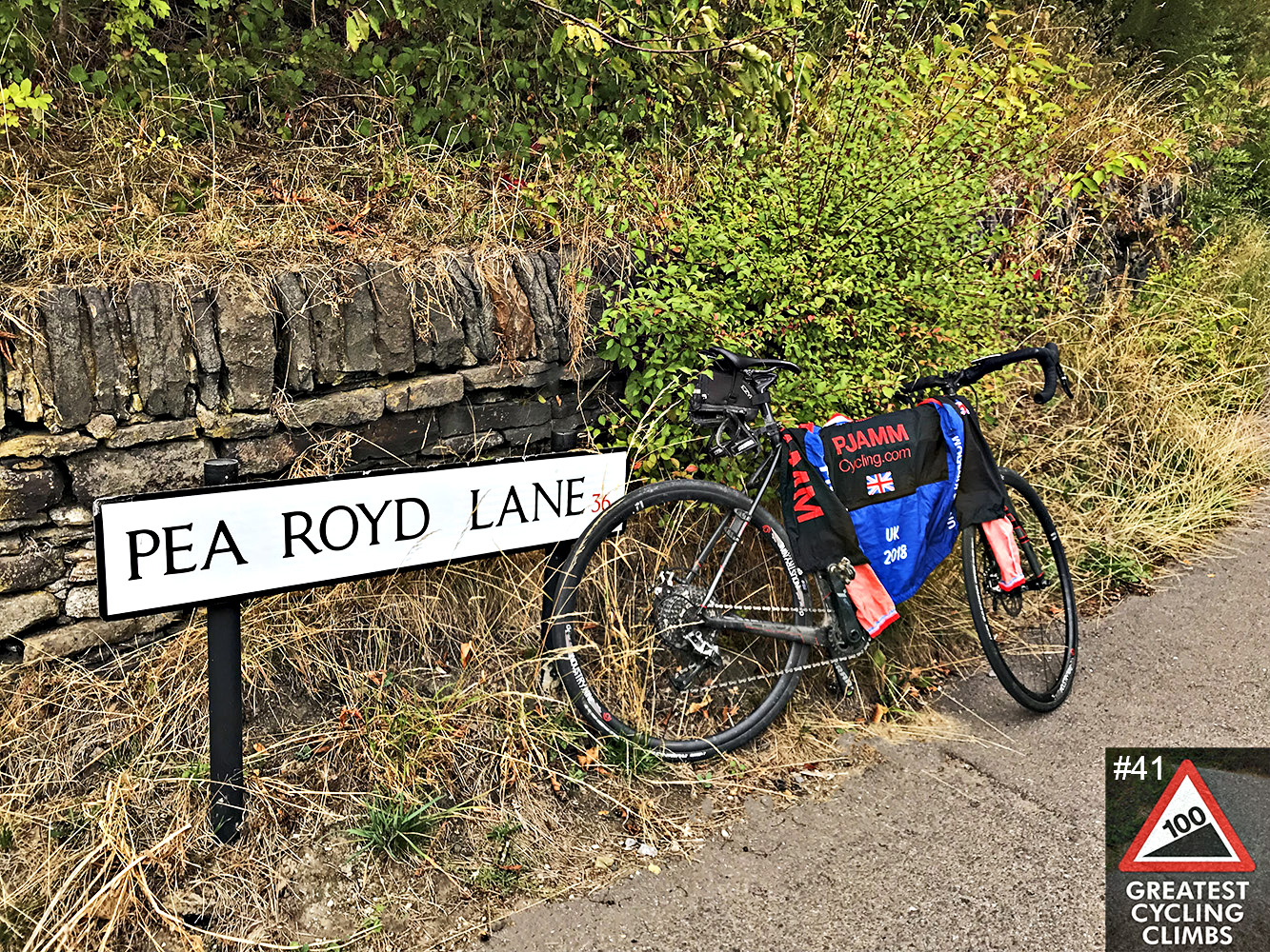 Cycling Pea Royd Lane - bike with PJAMM Cycling jersey draped over it, leaning against road sign for Pea Royd Lane, along brush covered stone fence line