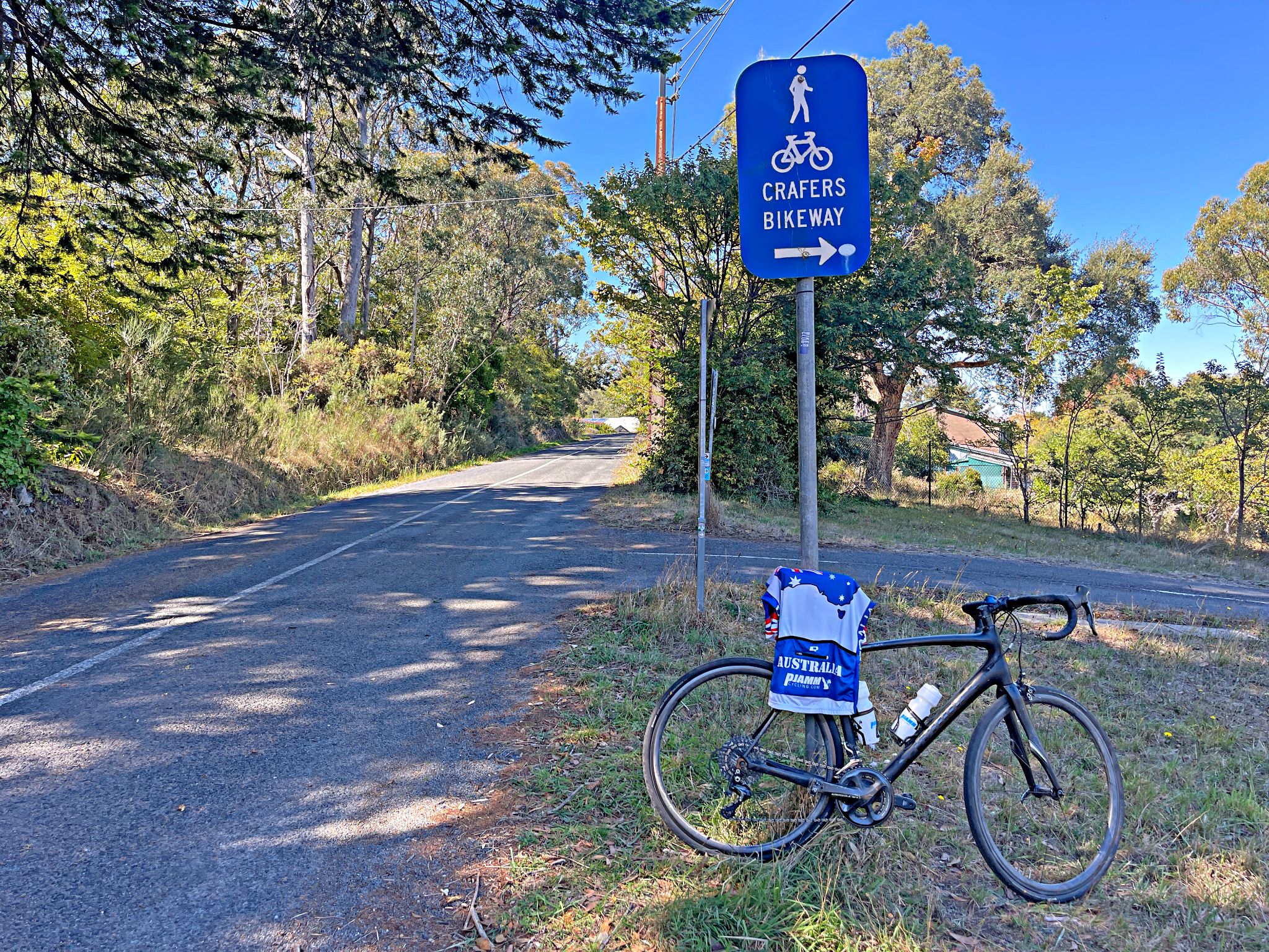 bike with PJAMM Cycling Australia jersey draped over it leans against roadsign for Crafers Bikeway; climb summit