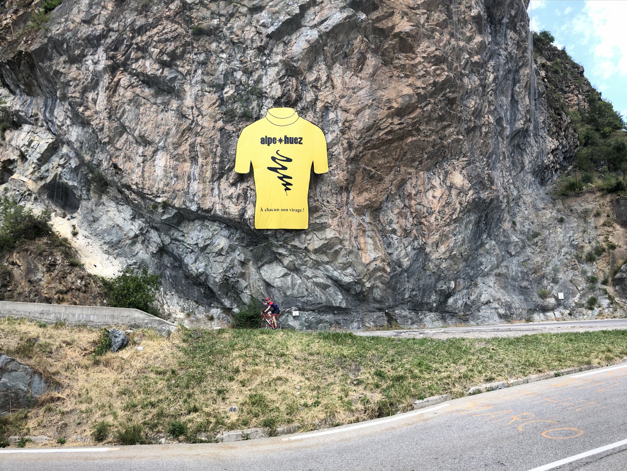 Cycling Alpe d'Huez - hairpin turn and yellow jersey on rock wall with cyclist riding past