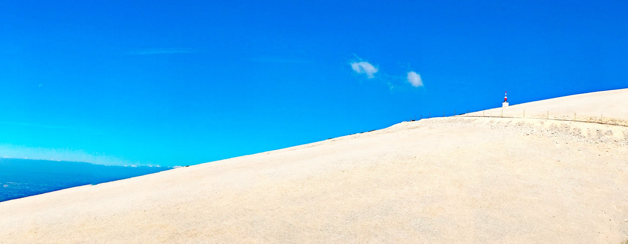 stark white limestone hillside with bright blue sky beyond, white and red tower can be seen at top of mountain