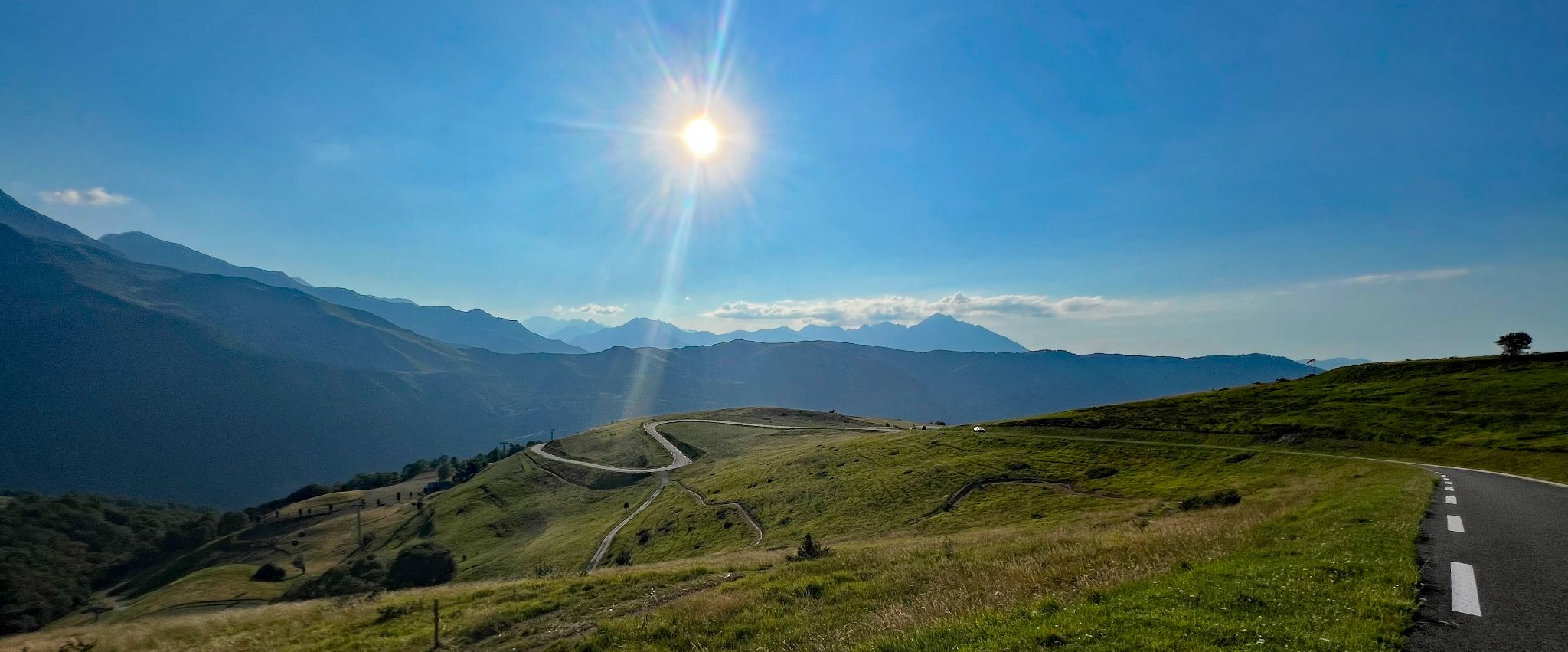 sun shines down over Station Peyragudes ride, France, winding roadway in hills in distance