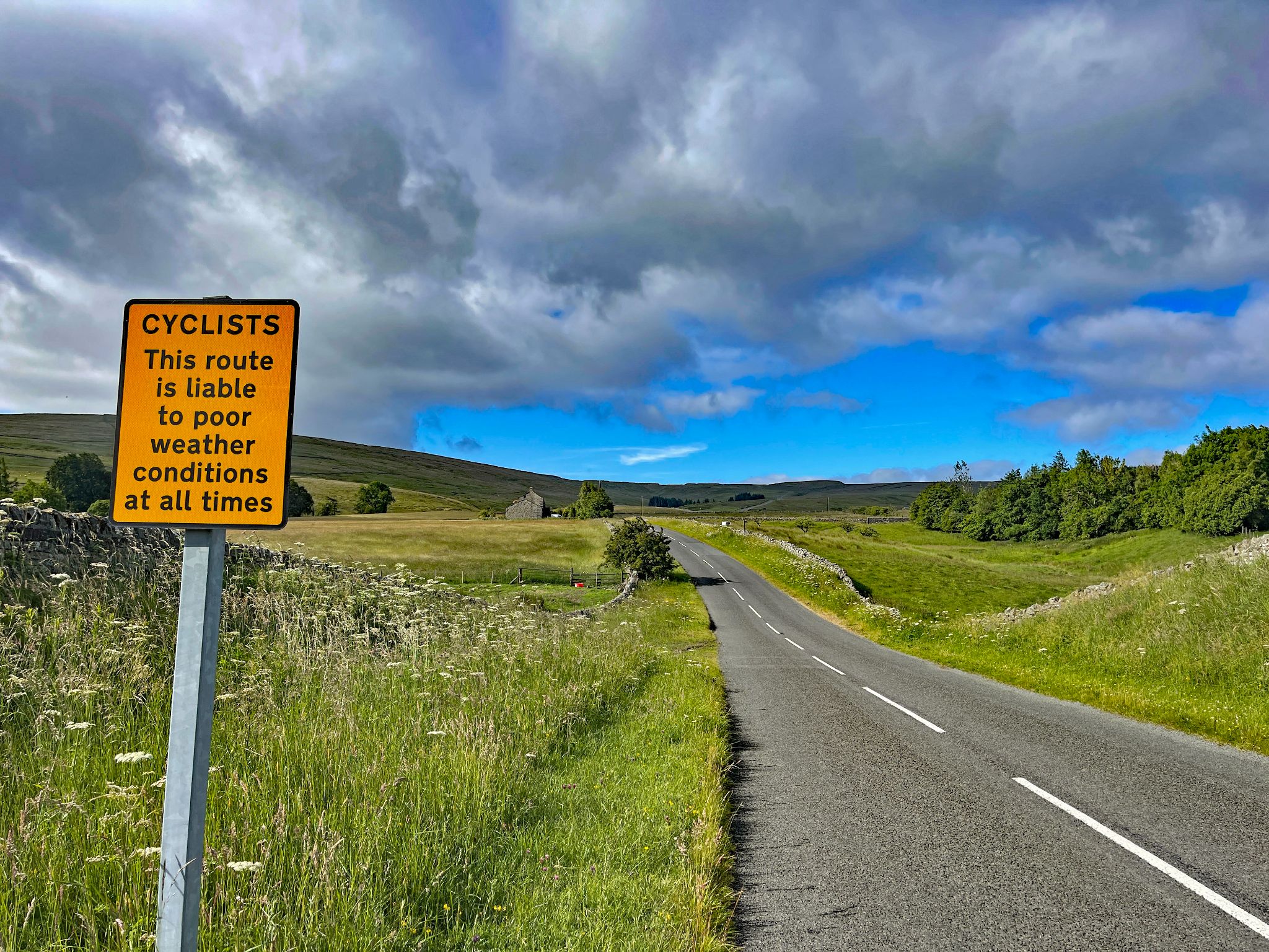 Yellow street sign reads "Cyclists: This route is liable to poor weather conditions at all times"