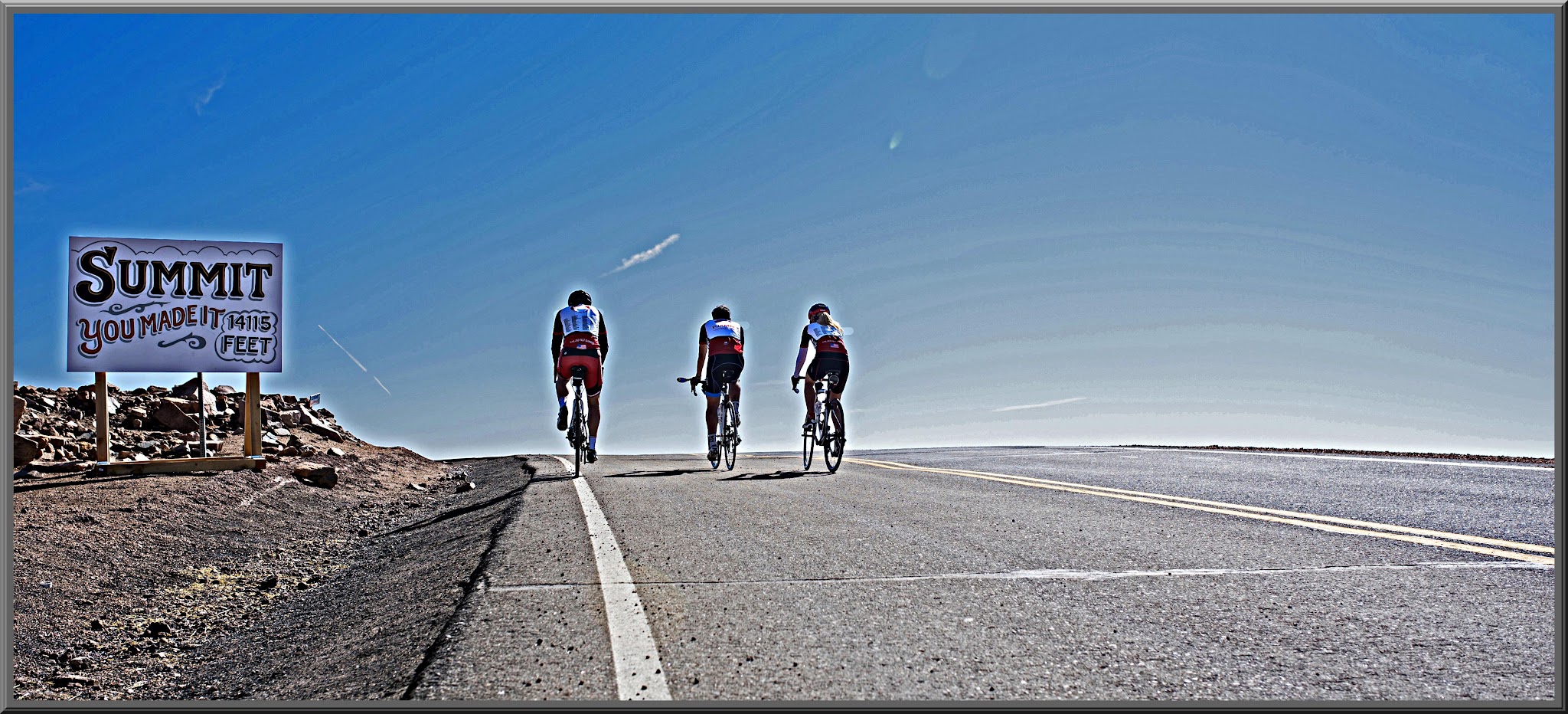 Cycling Pikes Peak  - three cyclists summiting Pikes Peak, summit sign reads "Summit, You Made It, 14,115 feet"
