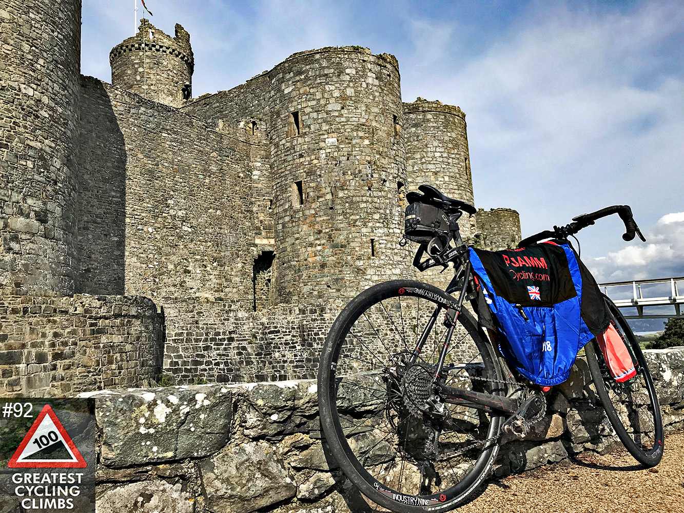 Cycling Ffordd Pen Llech, Wales - Simon Warren's 100 Greatest Cycling Climbs #92 logo in corner, bike parked in front of Harlech Castle, old stone castle