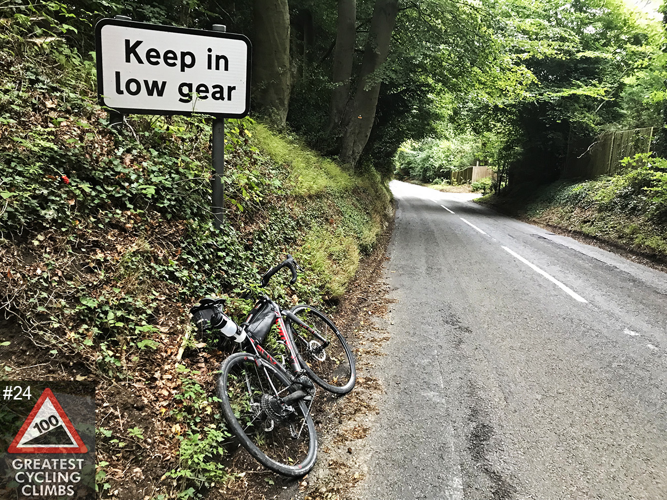 Cycling Streatley Hill - bike leaning against Keep in low gear sign; Simon Warren 100 Greatest Cycling Climbs logo