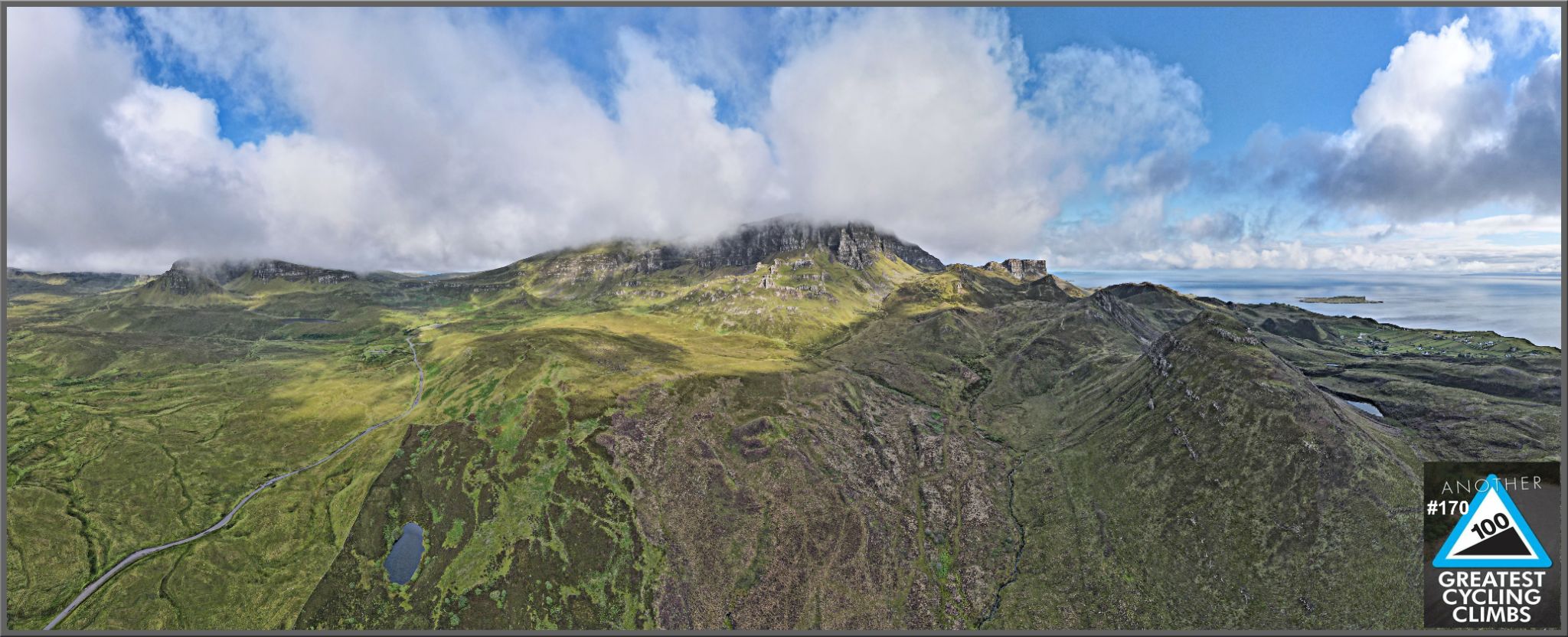 panoramic view of road snaking up green mountainside, bright blue skies