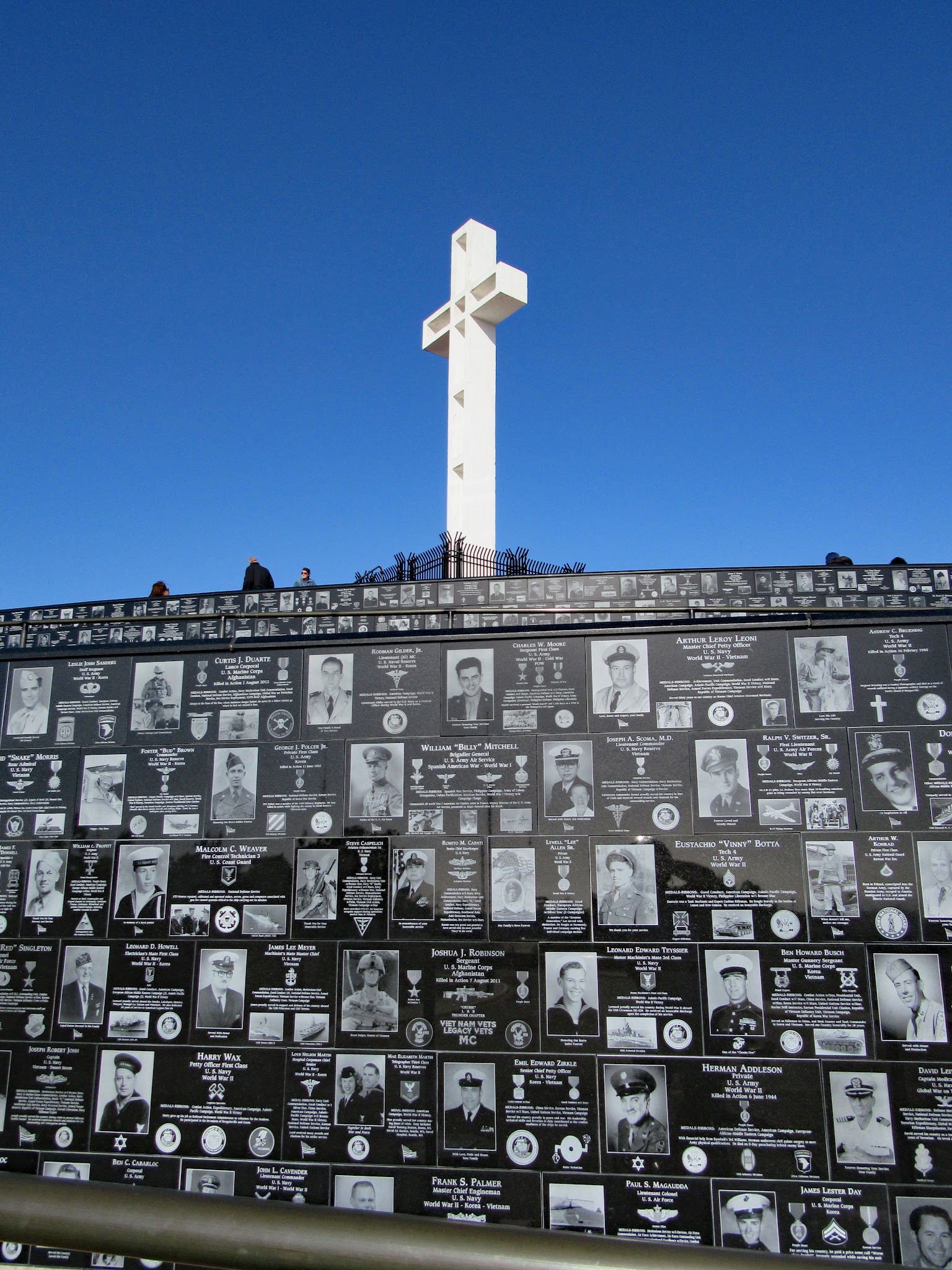 Veteran's memorial - large white cross and wall of black and white images of veterans