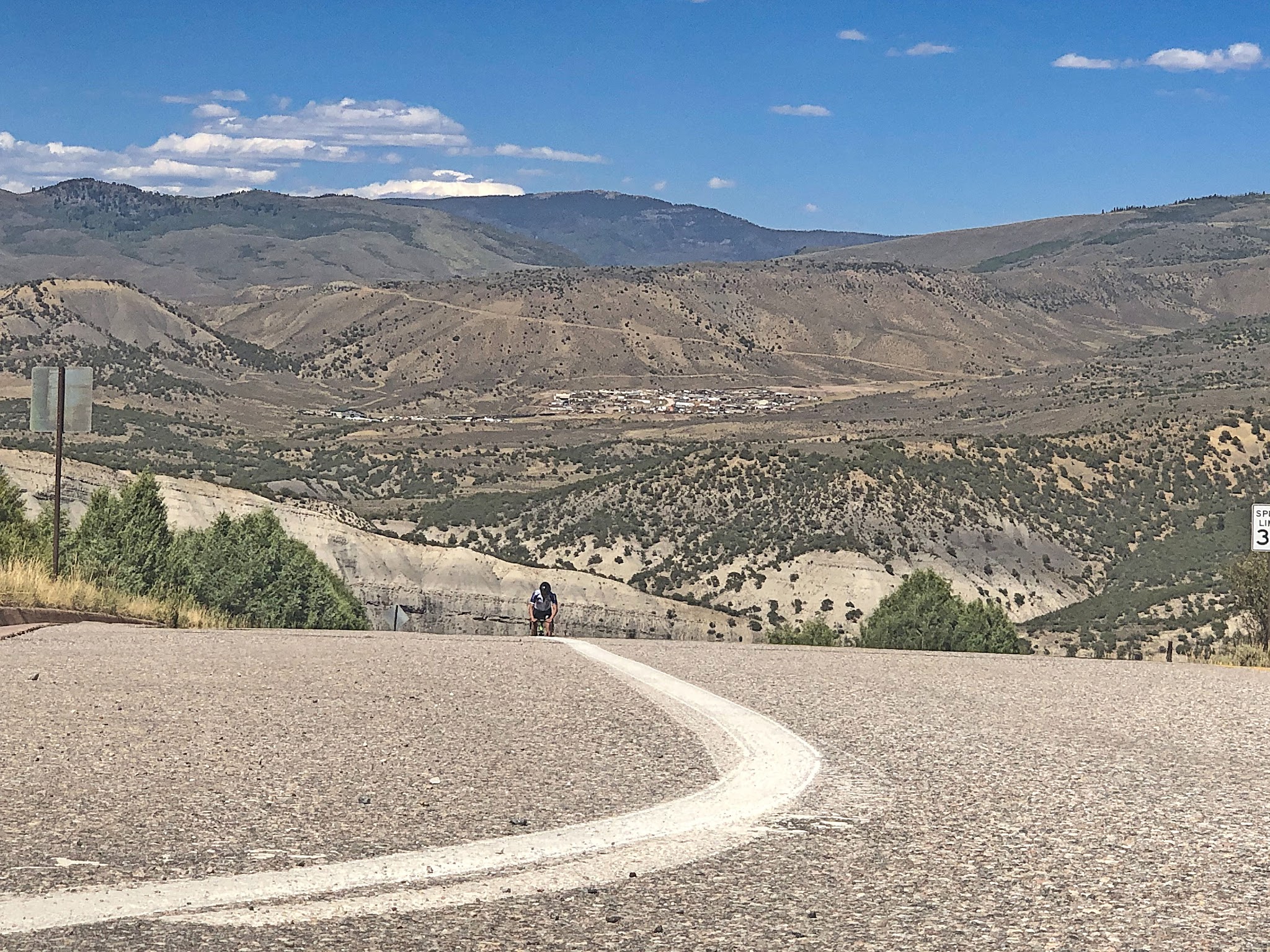 Cycling Bellyache Ridge, Colorado - cyclist climbing up two-lane roadway, dry, mountainous lands behind