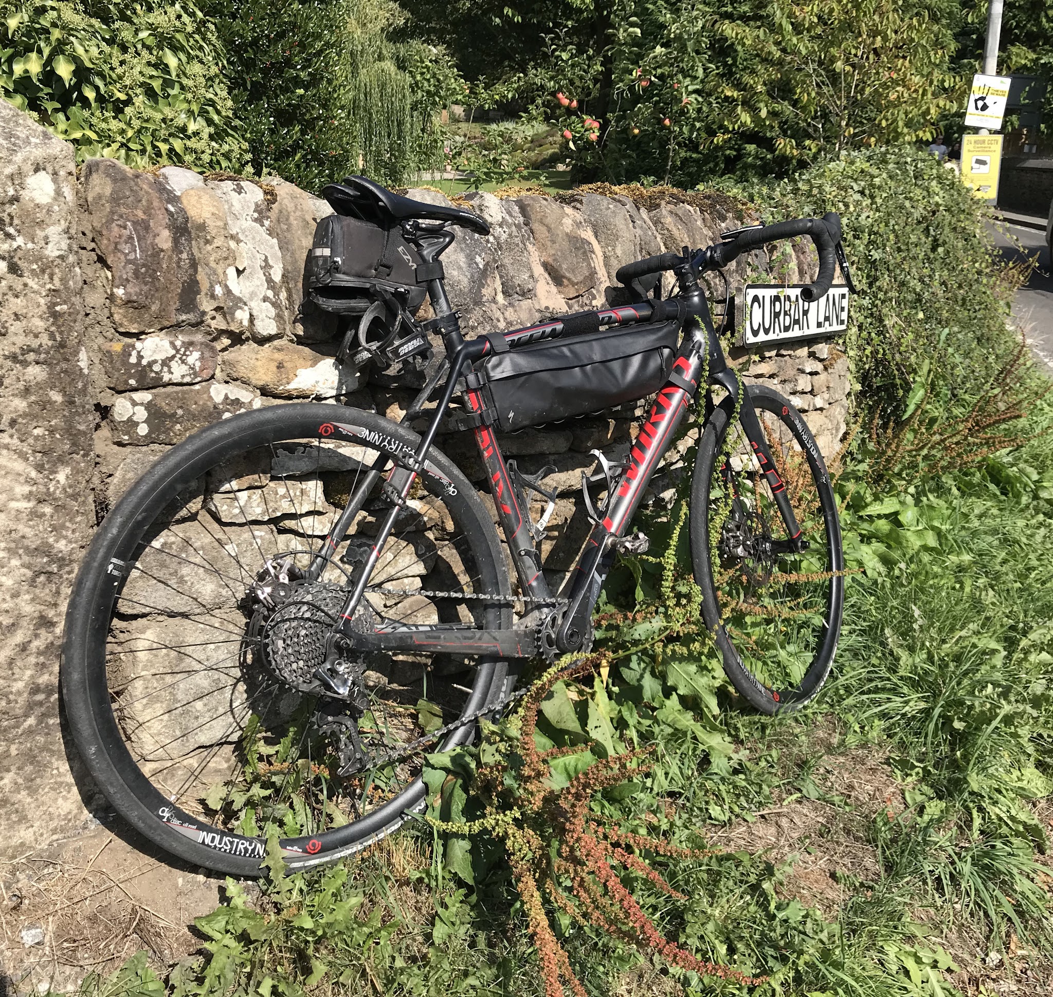 Cycling Curbar Edge, England - bike parked along stone fence in greenery, road sign for Curbar Lane