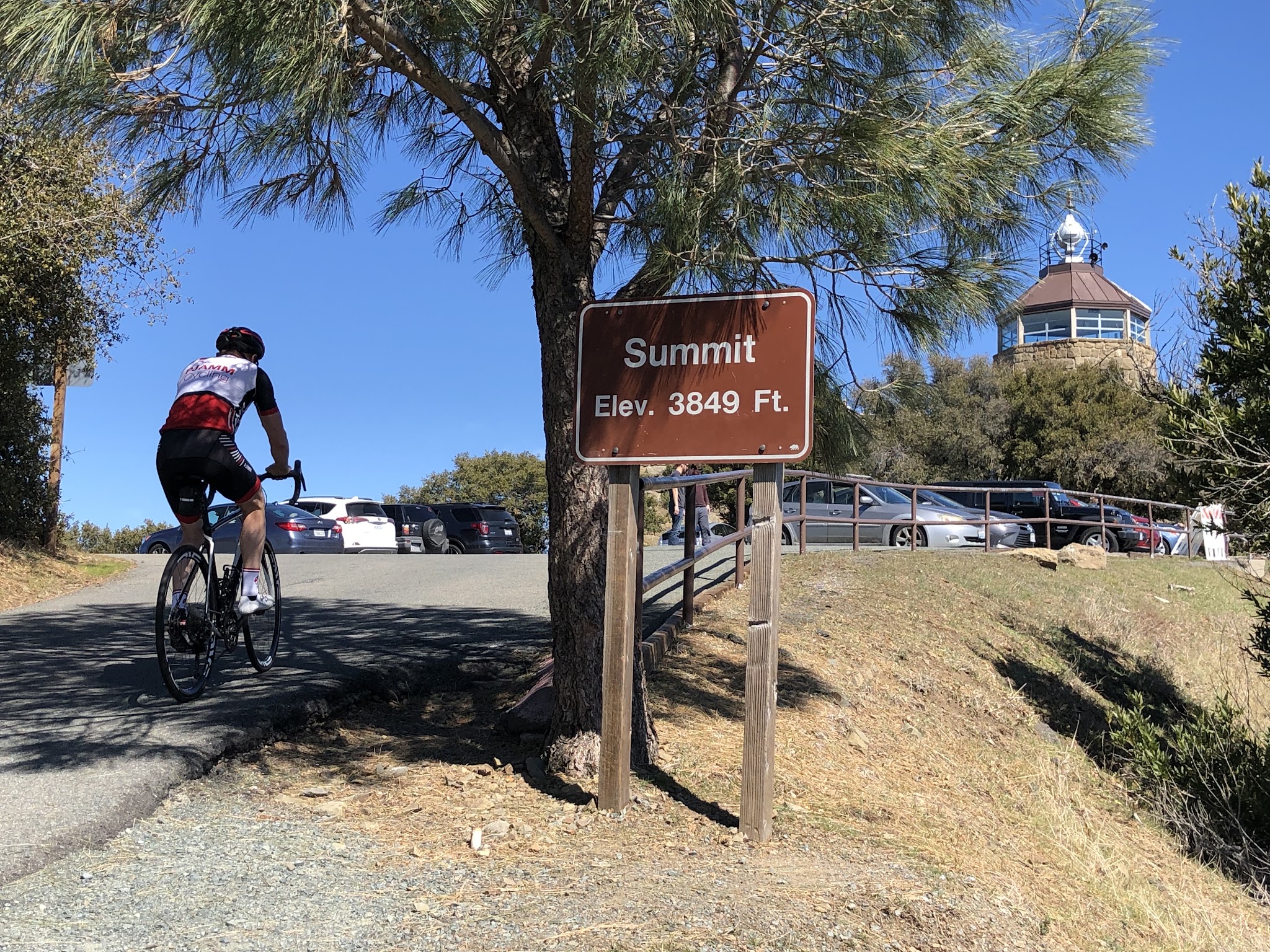Cycling Mt. Diablo - cyclist on bike riding past summit sign - visitor center and beacon