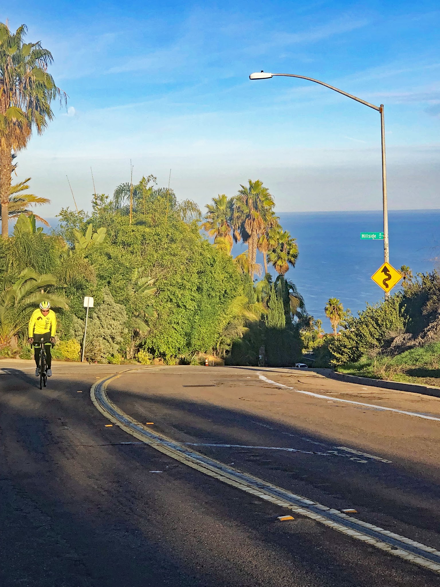 cyclist climbs on two-lane roadway on the steepest portion of the ride, at climb's beginning, Pacific Ocean in background