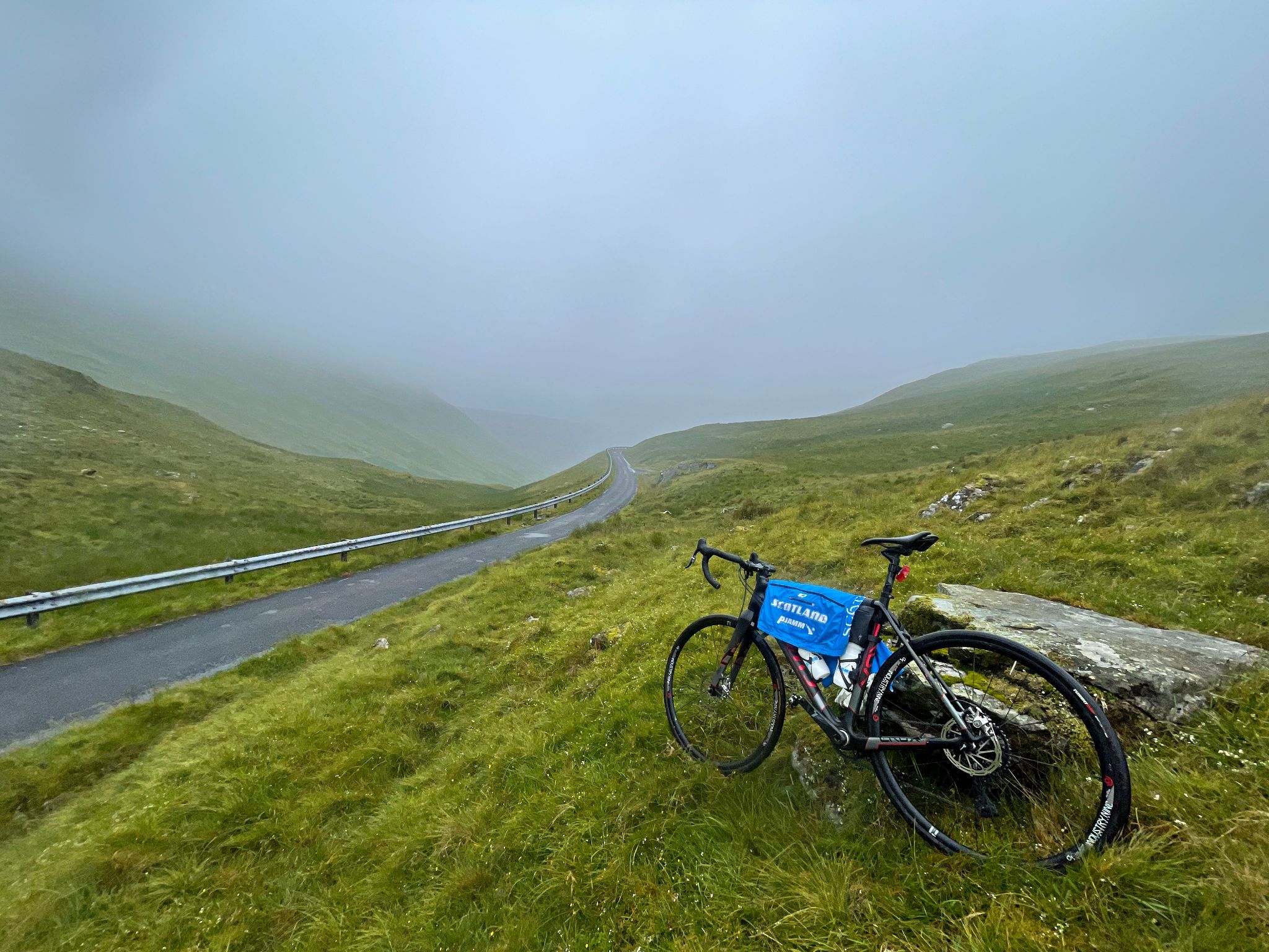 bike parked against stone in green hillside at climb finish, foggy day 