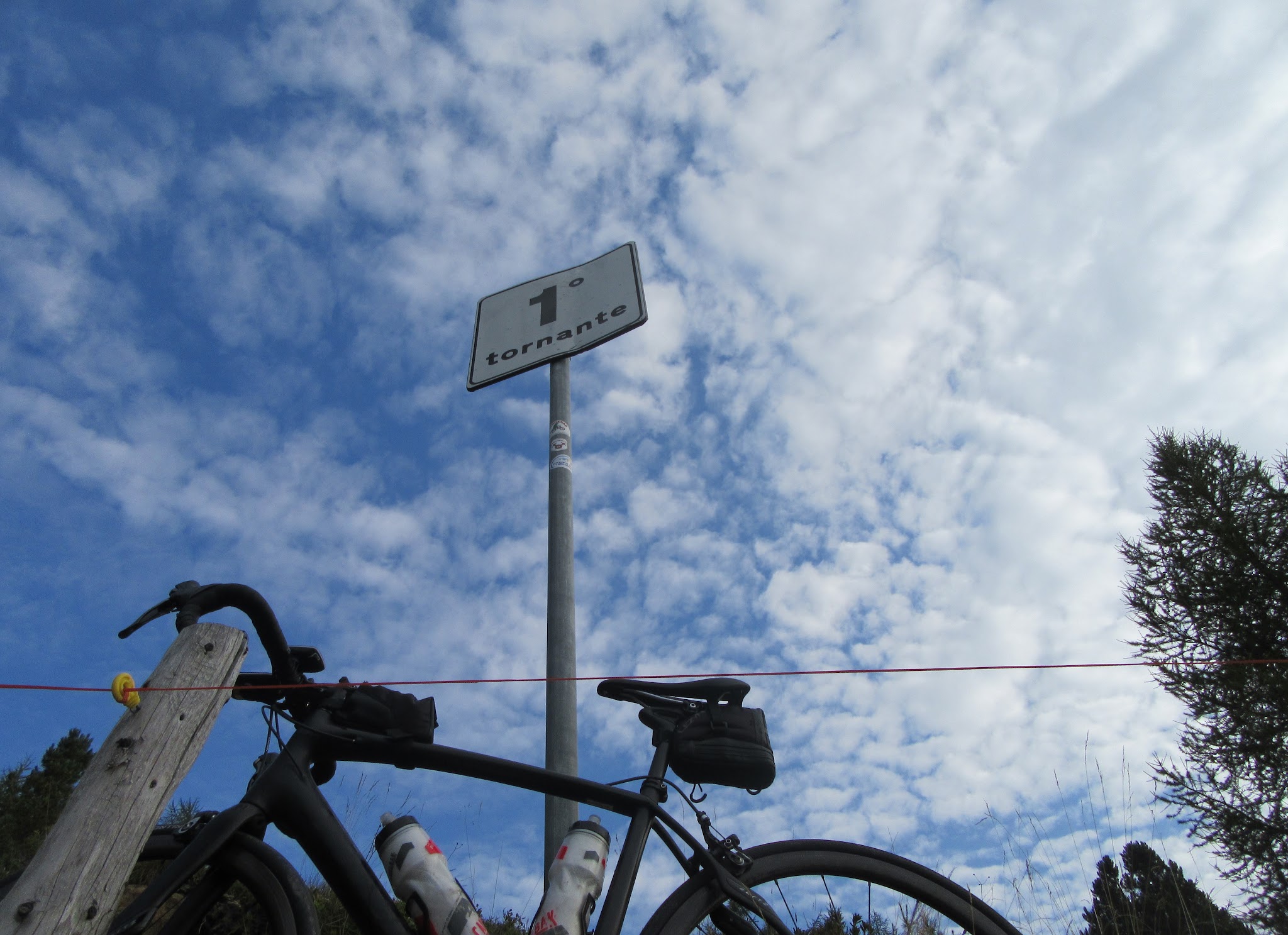 Cycling Passo del Mortirolo from Mazzo di Valtellina - Tornanti (hairpin) #1 sign with bike leaning against sign