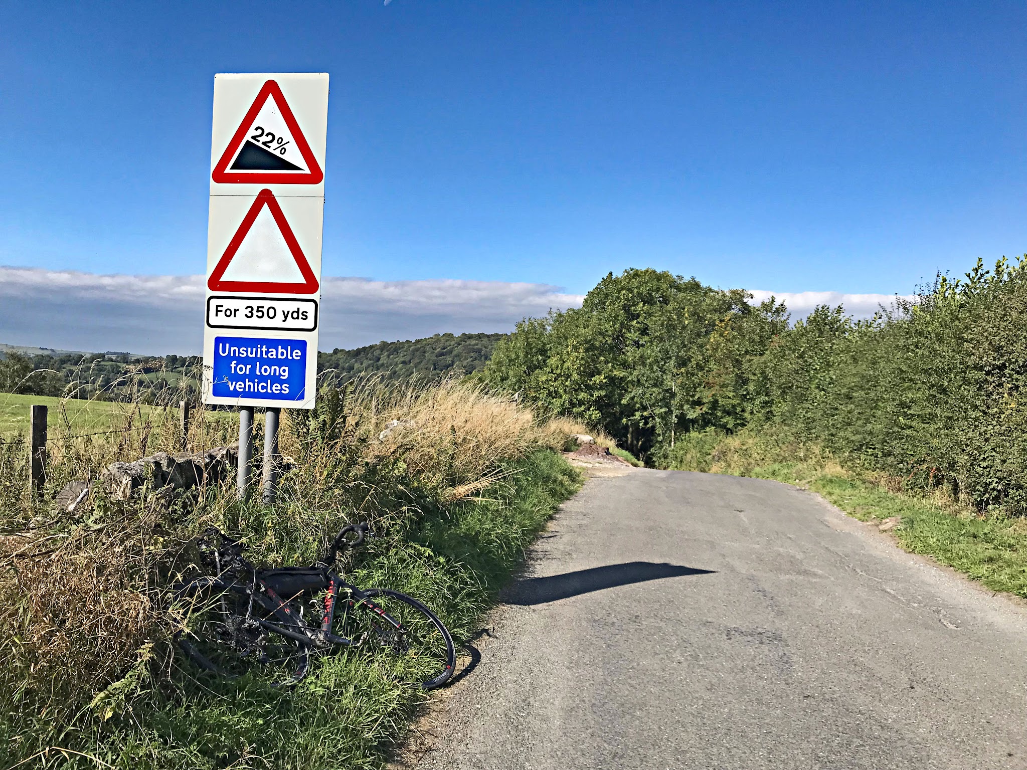 Cycling Riber, England - view 50 meters from climb finish, one-lane road surrounded by thick vegetation, road sign for 22% grade, unsuitable for long vehicles 