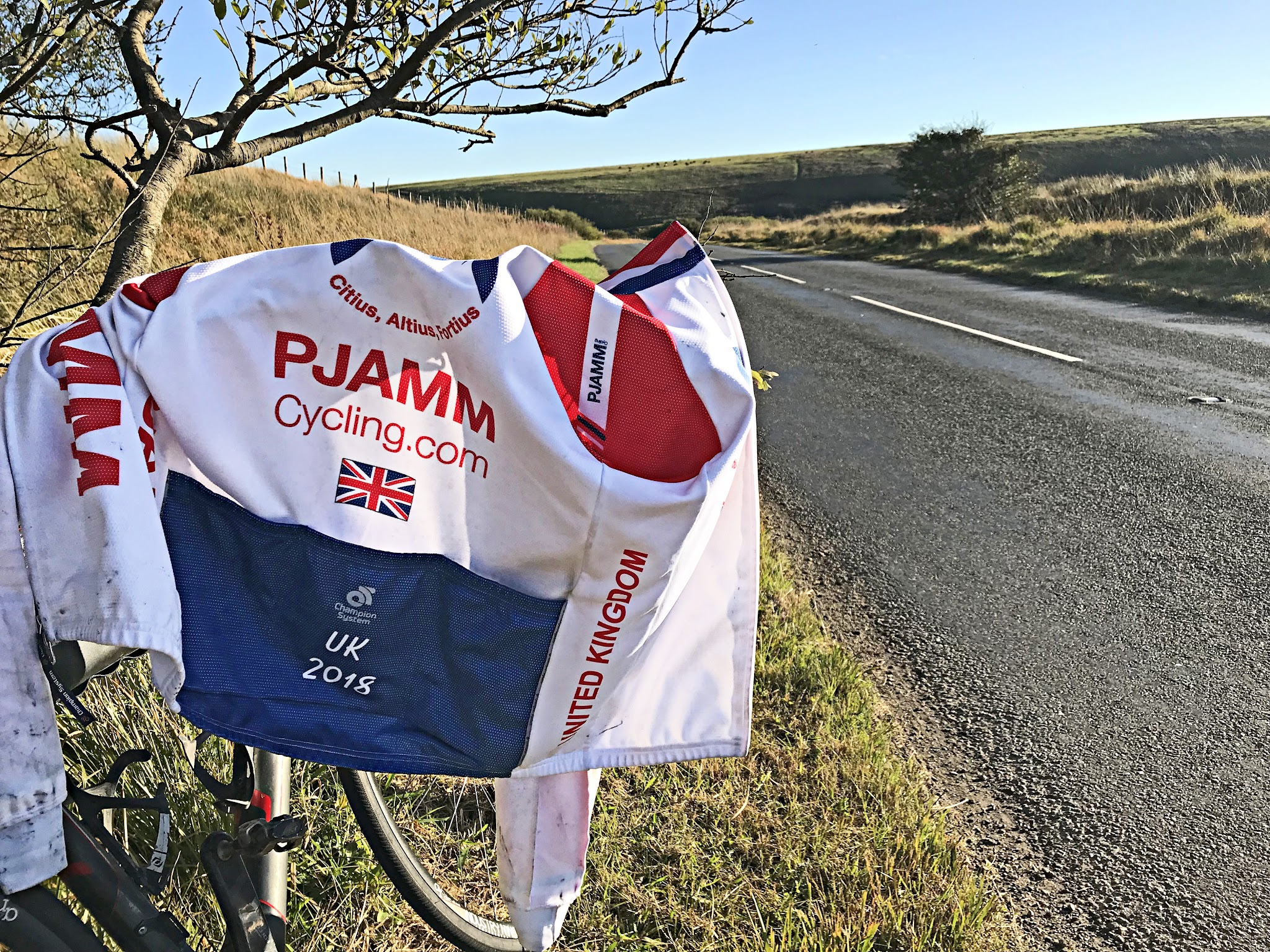 Cycling Exmoor Forest, England - PJAMM Cycling UK 2018 jersey propped atop bike parked along side of two lane roadway on hillside
