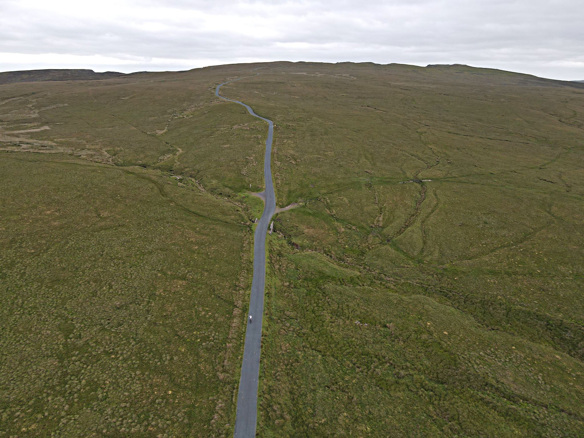 aerial drone view shows roadway cutting straight path through otherwise unobstructed brown-green pastureland