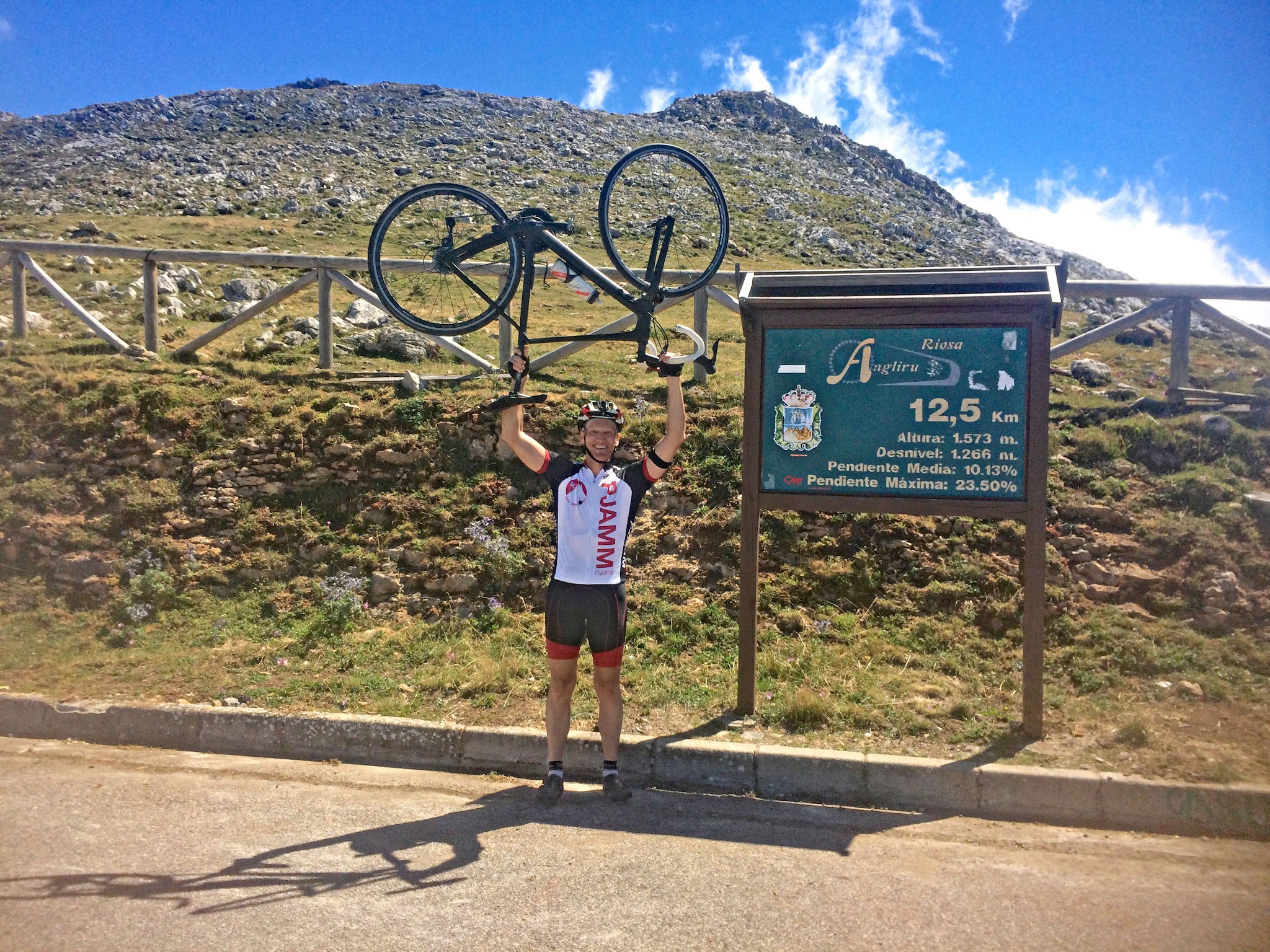 Cycling Alto de l'Angliru, Spain -  PJAMM Cyclist Ron Hawks holds his bike over his head at summit of Angliru next to summit sign