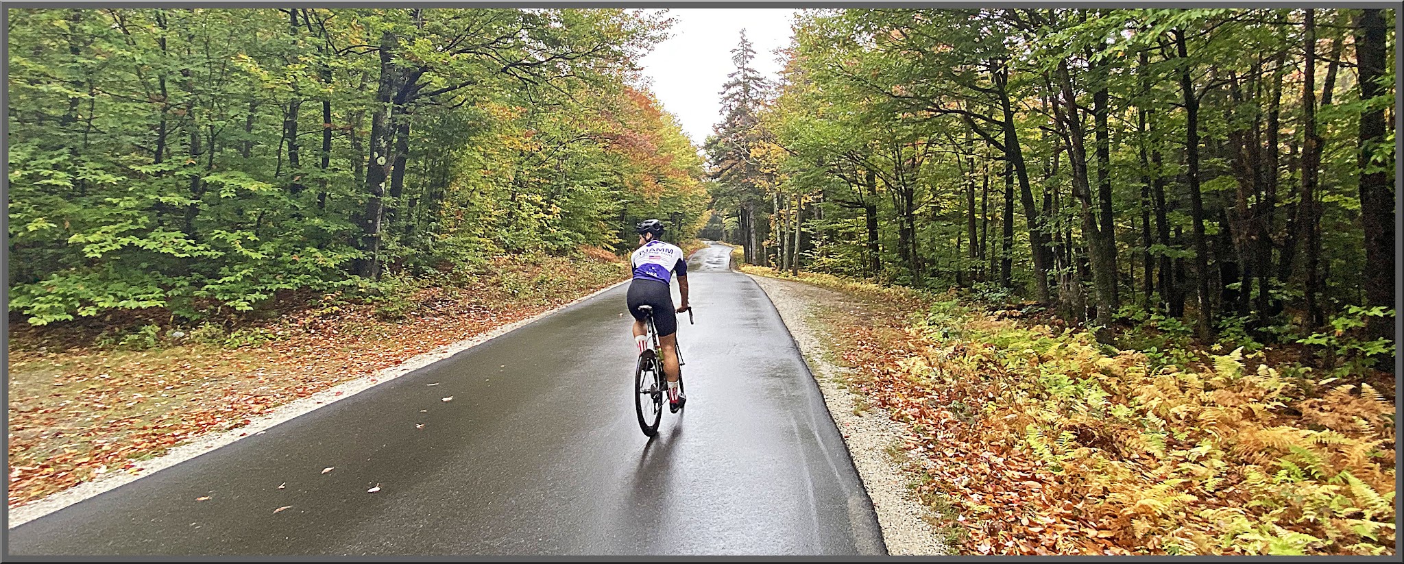 Cycling Hurricane Mountain Road West, New Hampshire - cyclist climbs on wet, one-lane roadway surrounded by green trees and forestation