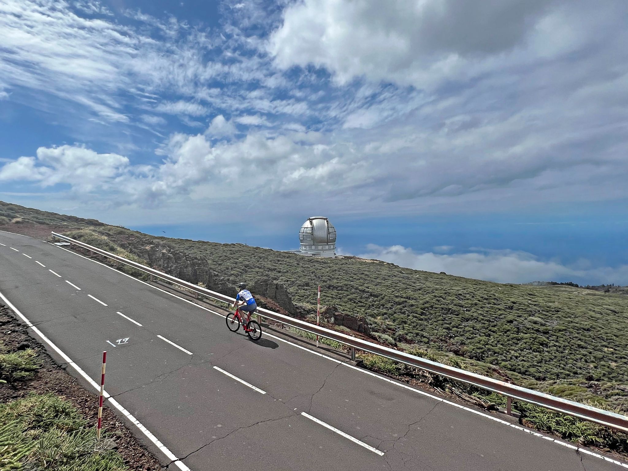 PJAMM cyclist rides on two-lane roadway with Gran Telescopio Canarias in distance 