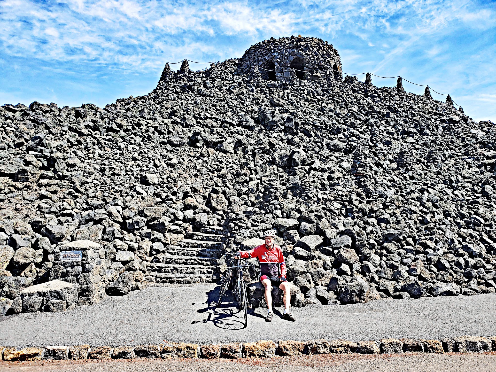 Cycling McKenzie Pass West - cyclist sitting at summit with bike, lava field