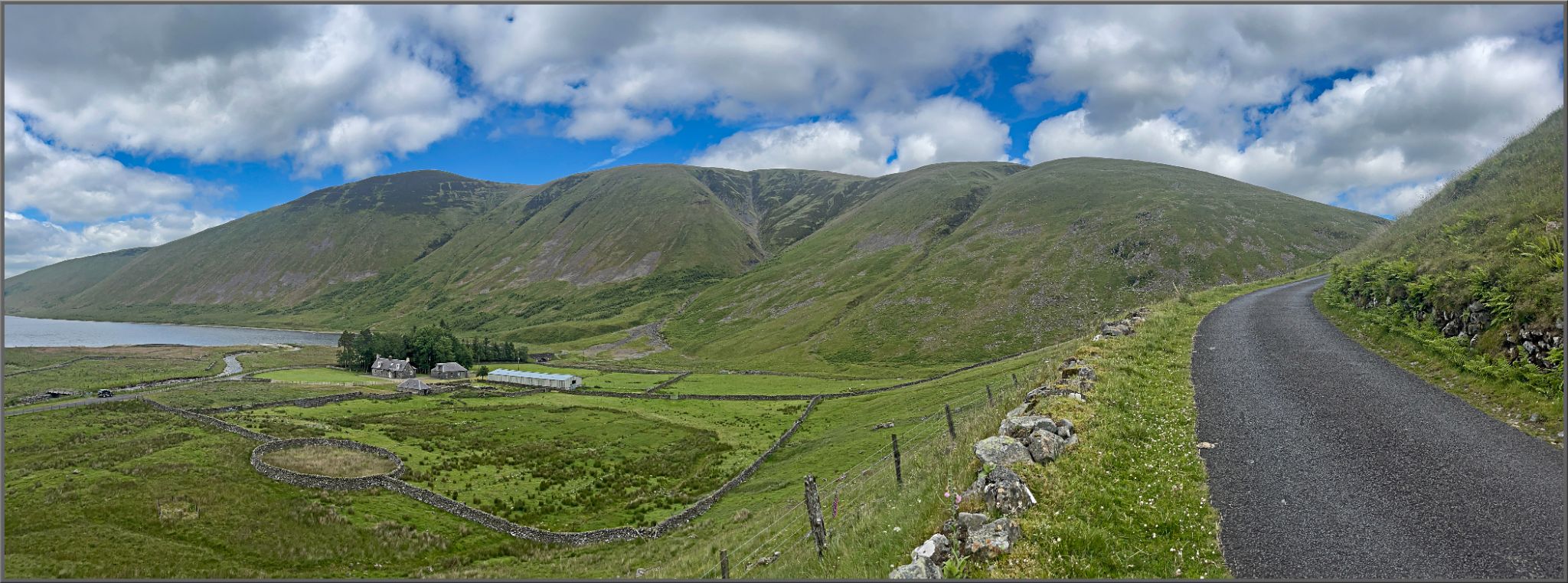 panoramic view of green hillsides, blue sky, pond in distance