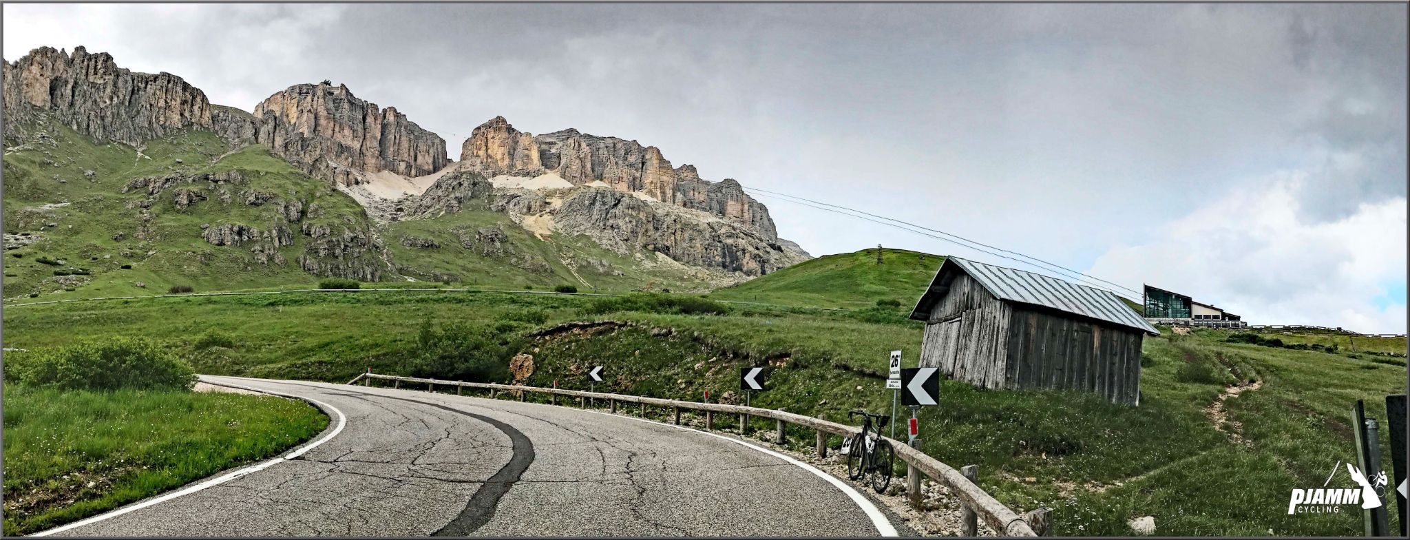 Cycling Passo Pordoi from Canazei - Italian countryside, bike parked on roadside next to old farm building 