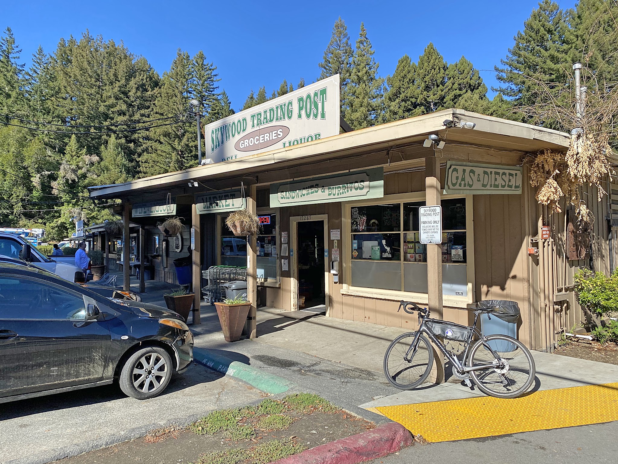 Cycling Old La Honda Road, California - cars and bikes parked in front of building with sign reading "Skywood Trading Post"