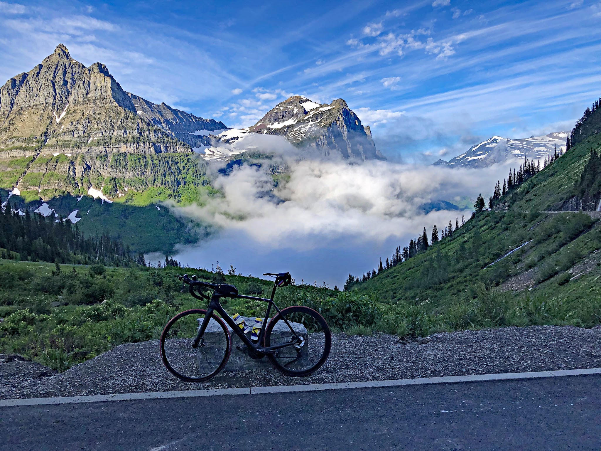 Cycling Logan Pass West, Going-to-the-Sun Road, Glacier National Park  - bike parked along side of road overlooking sharp and steep mountain peaks, fog in center-ground