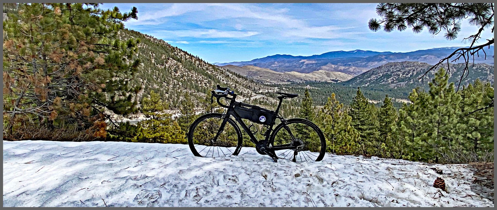 Cycling Old Clear Creek Road, NV - bike parked in snow on roadside overlooking mountains covered in pine trees