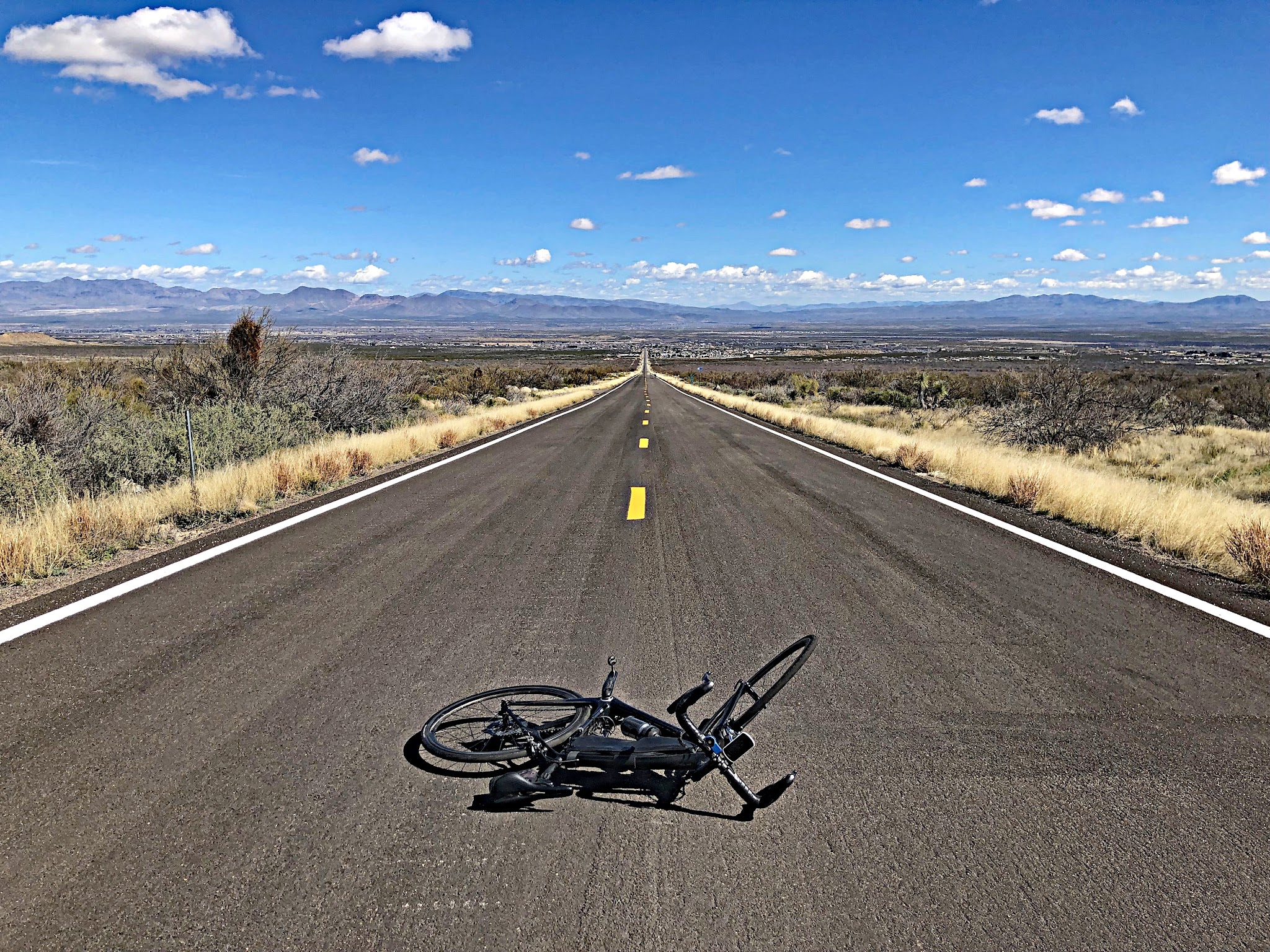 Cycling Mt. Graham, Arizona - bike parked in center of dead straight 2-lane roadway, high desert surroundings, blue sky with small white clouds