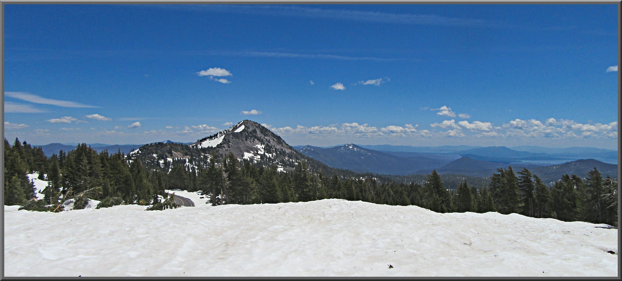 Cycling Mt. Lassen North, California - thick snow covered ground in foreground, overlooking snow capped mountains, blue sky, clouds