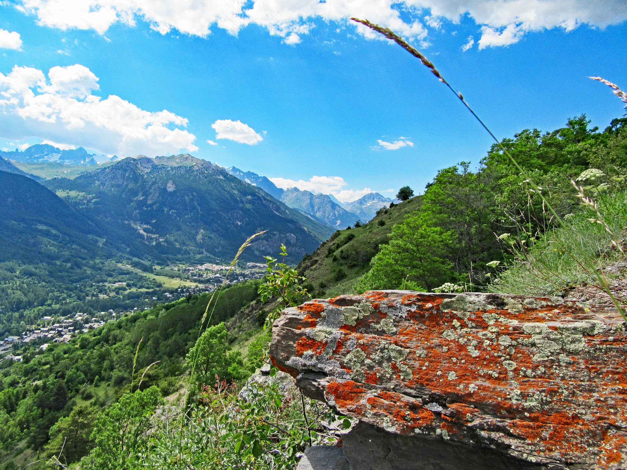 Cycling Col du Granon - view looking over lush green mountains, bright blue sky, large stone with red moss growing on it