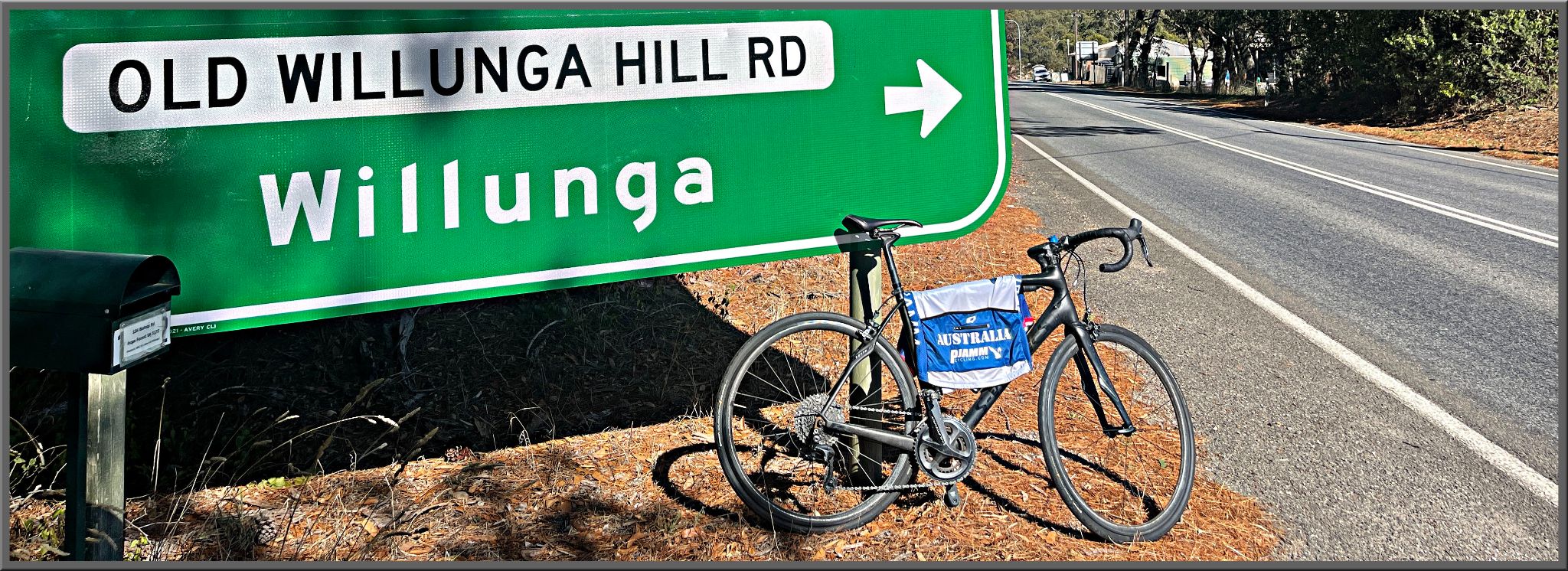 Cycling Old Willunga Hill Road, South Australia bike parked next to large green road sign for Old Willunga Hill Road