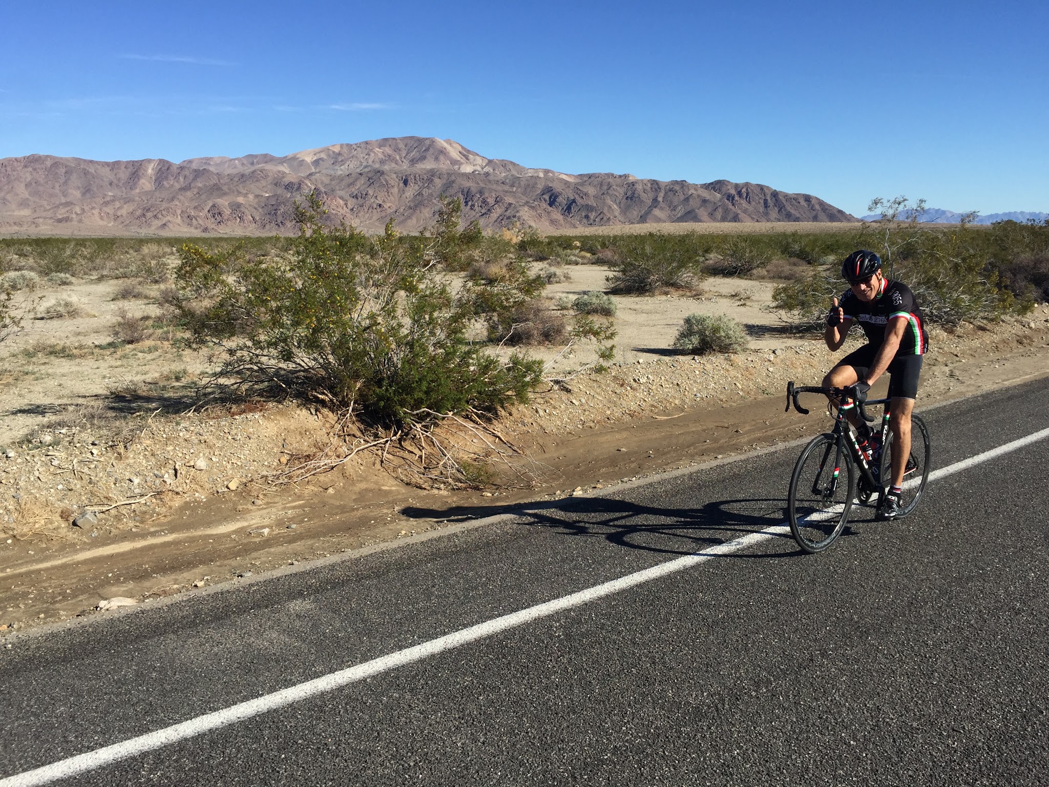 Cycling Joshua Tree National Park, California - cyclist on roadway riding Pinto Basin Road North, desert scrub brush landscape behind him