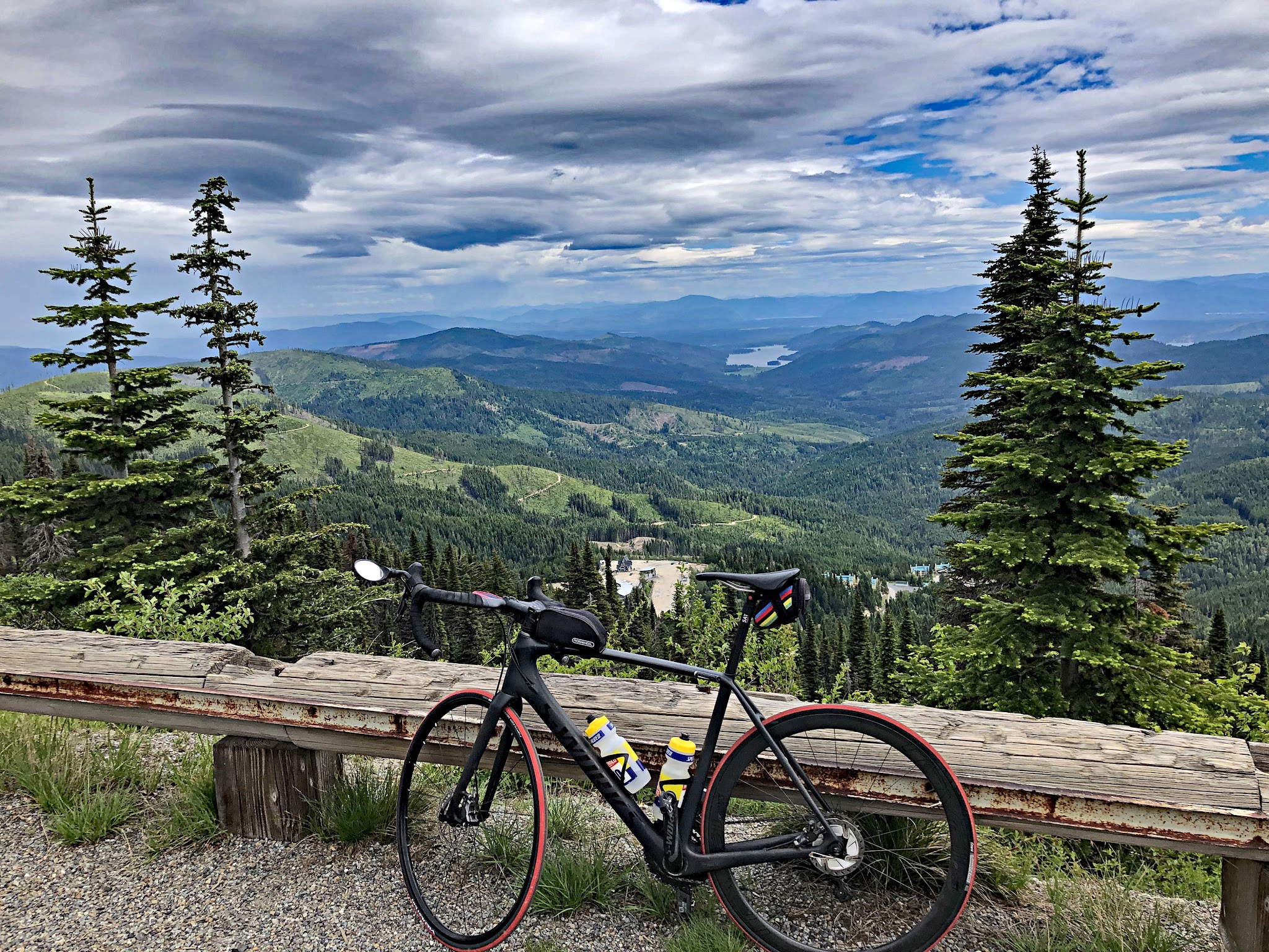 Cycling Mt. Spokane, Washington - bike parked at viewpoint against low wooden fence overlooking green hillsides toward Idaho and Twin Lakes