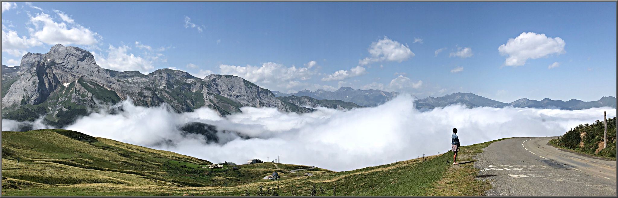 Cycling Col d’Aubisque from Laruns - panoramic view of two lane roadway, mountain tops in background, white clouds surrounding roadway
