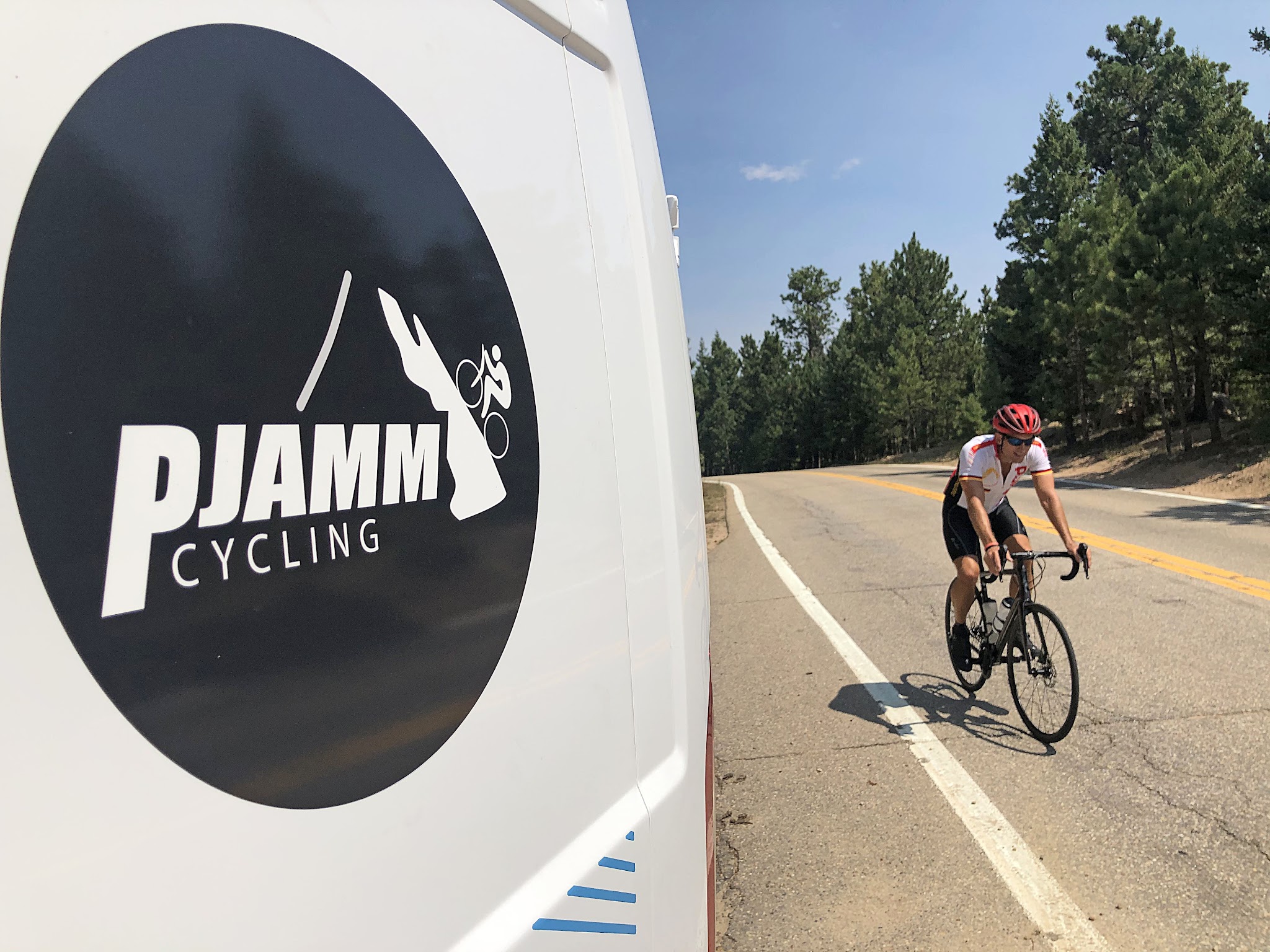 Cycling Super Duper Flag, Boulder, Colorado - close up of decal on PJAMM Cycling SAG vehicle, cyclist riding on roadway next to van