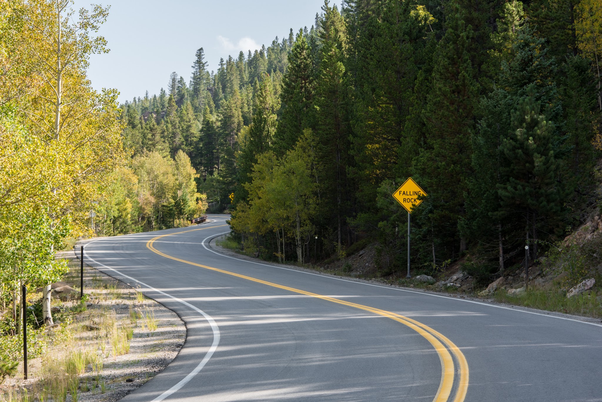 Cycling Juniper Pass West - gentle curves along two-lane roadway lined with dense forestation, road sign reading Falling Rock