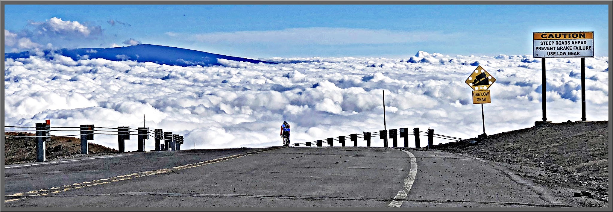 Cycling Mauna Kea, Hawaii - cyclist climbing Mauna Kea, above the cloudline, Mauna Loa can be seen in the distance