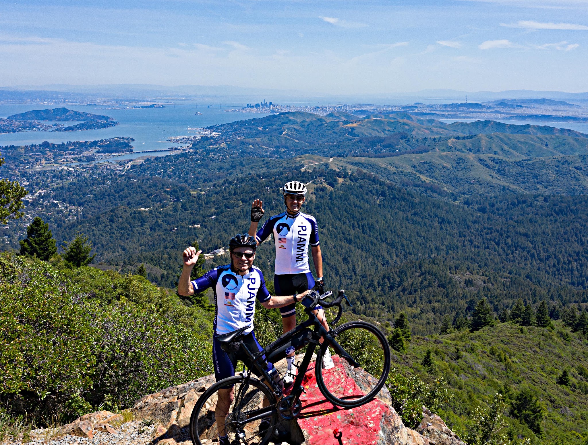 Cycling Golden Gate Bridge to Mt. Tam, California Cycling Golden Gate Bridge to Mt. Tam, California - two PJAMM Cyclists stand with bikes on rock formation on Mt. Tam's west peak, San Francisco, Angel Island, and the Bay Bridge can be seen in background