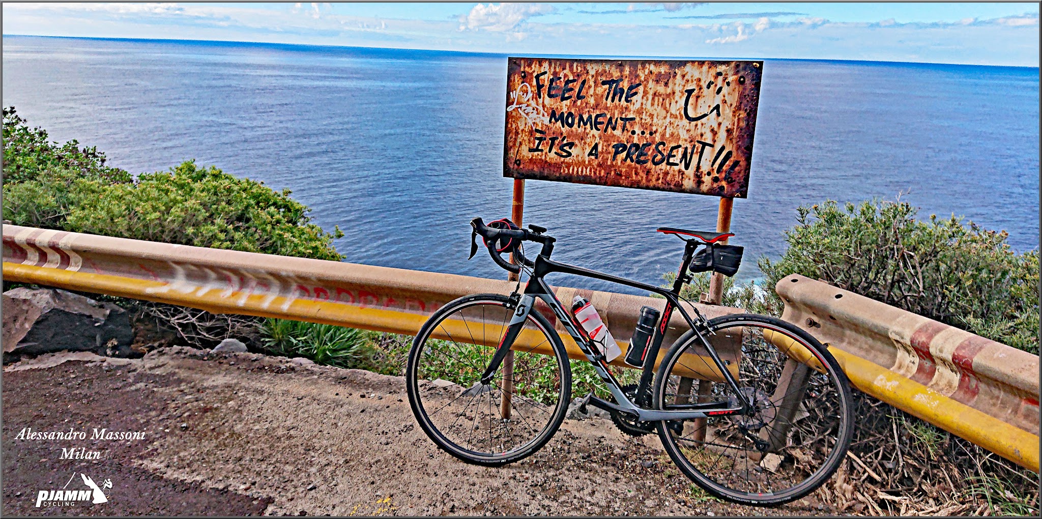 Cycling Llano de las Animas, Spain - bike parked against guardrail overlooking ocean next to rusty sign that reads "Feel the moment...it's a present!!" with a smiley face