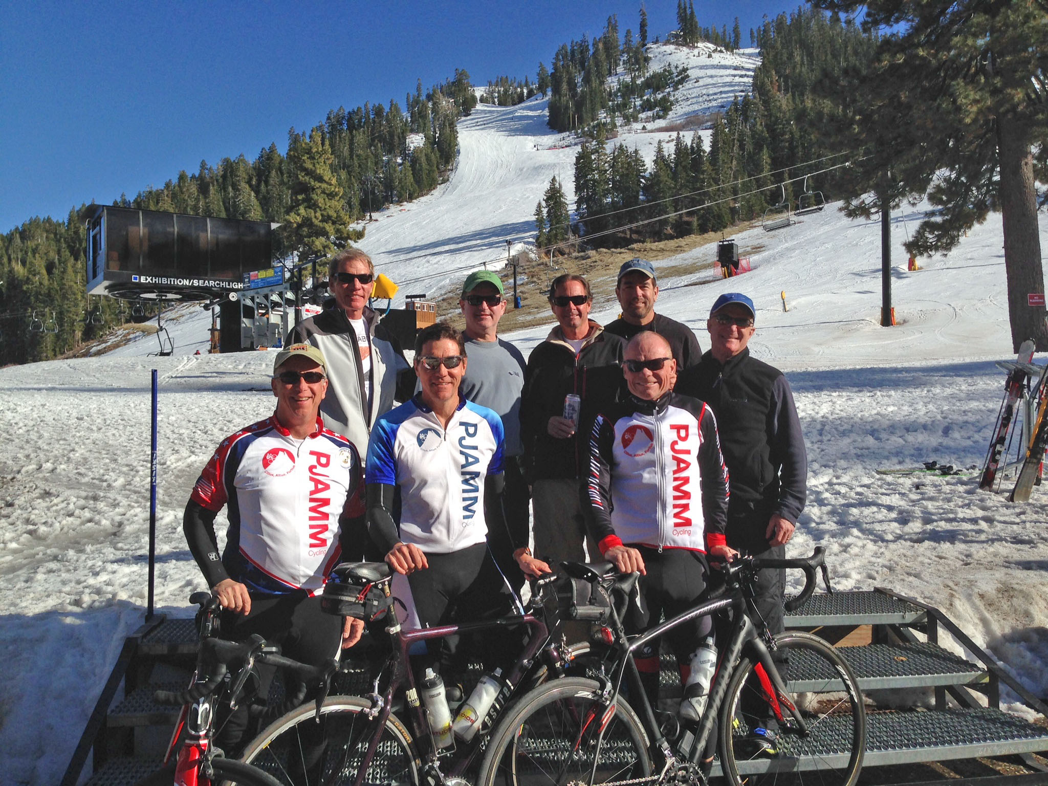 group of PJAMM Cyclists pose with bikes at base of ski runs on snowy hillsides